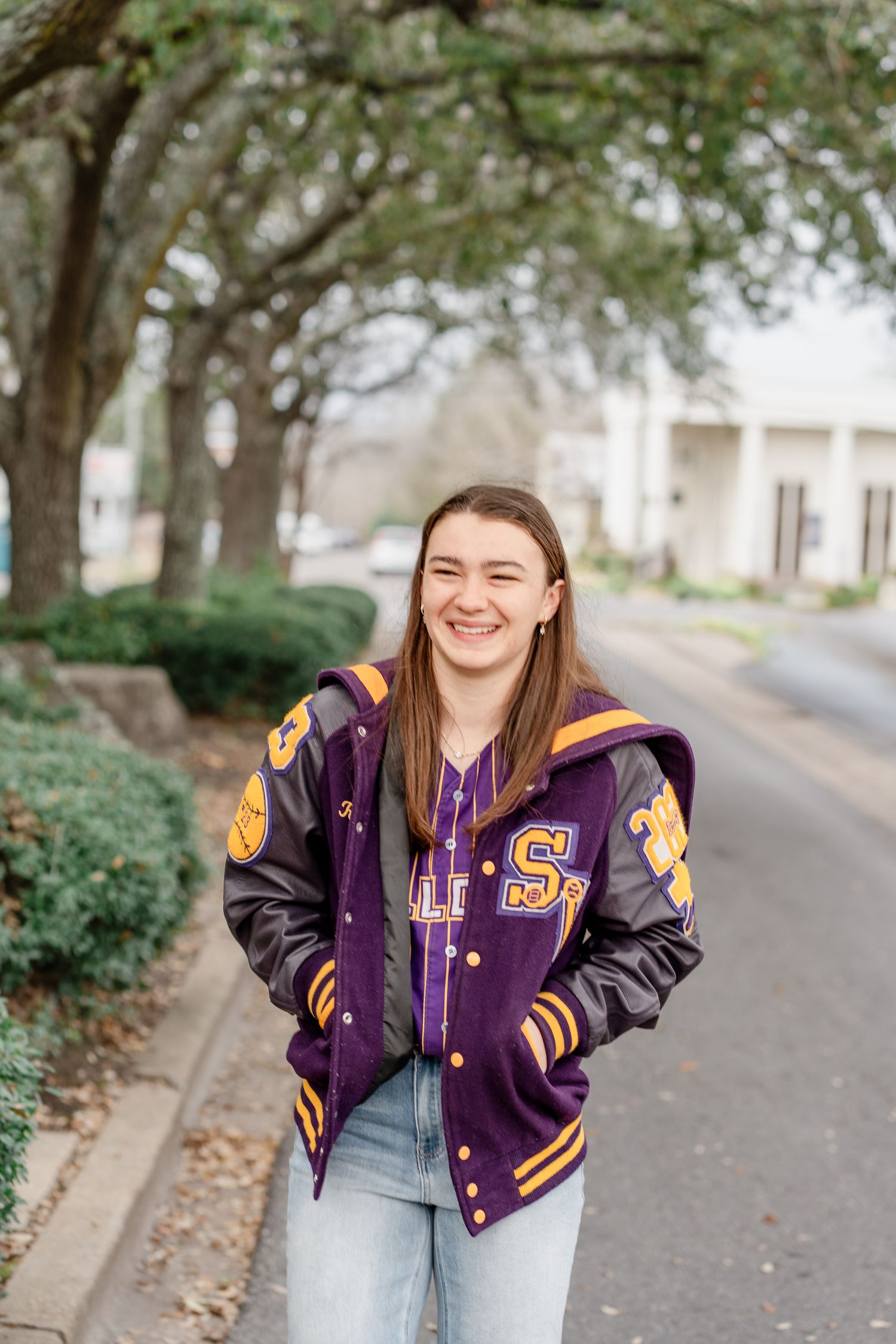 Casual outdoor photo session featuring purple and gold varsity jacket with light denim.