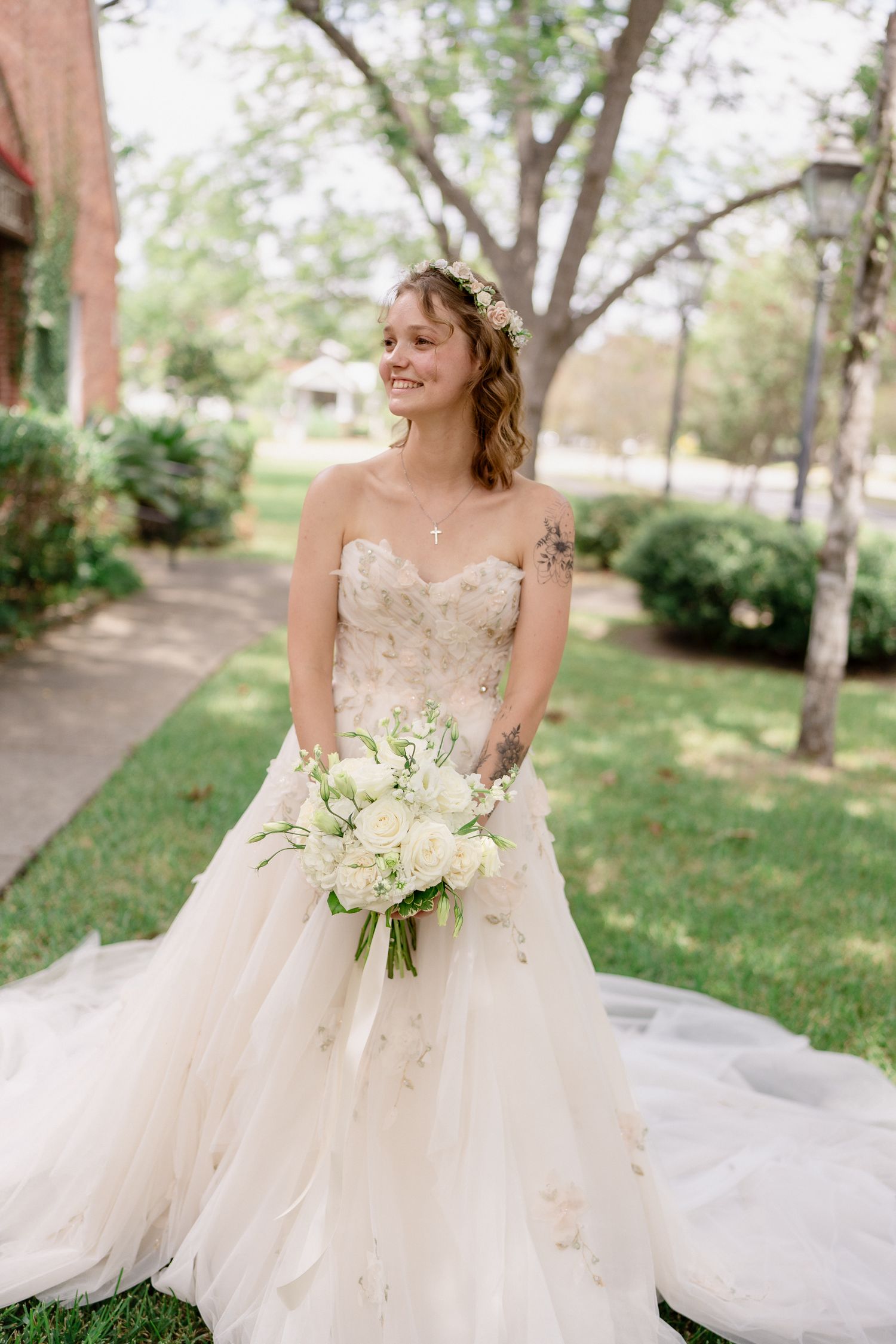 A bride in a delicate tulle gown holds a white floral bouquet in a garden setting.