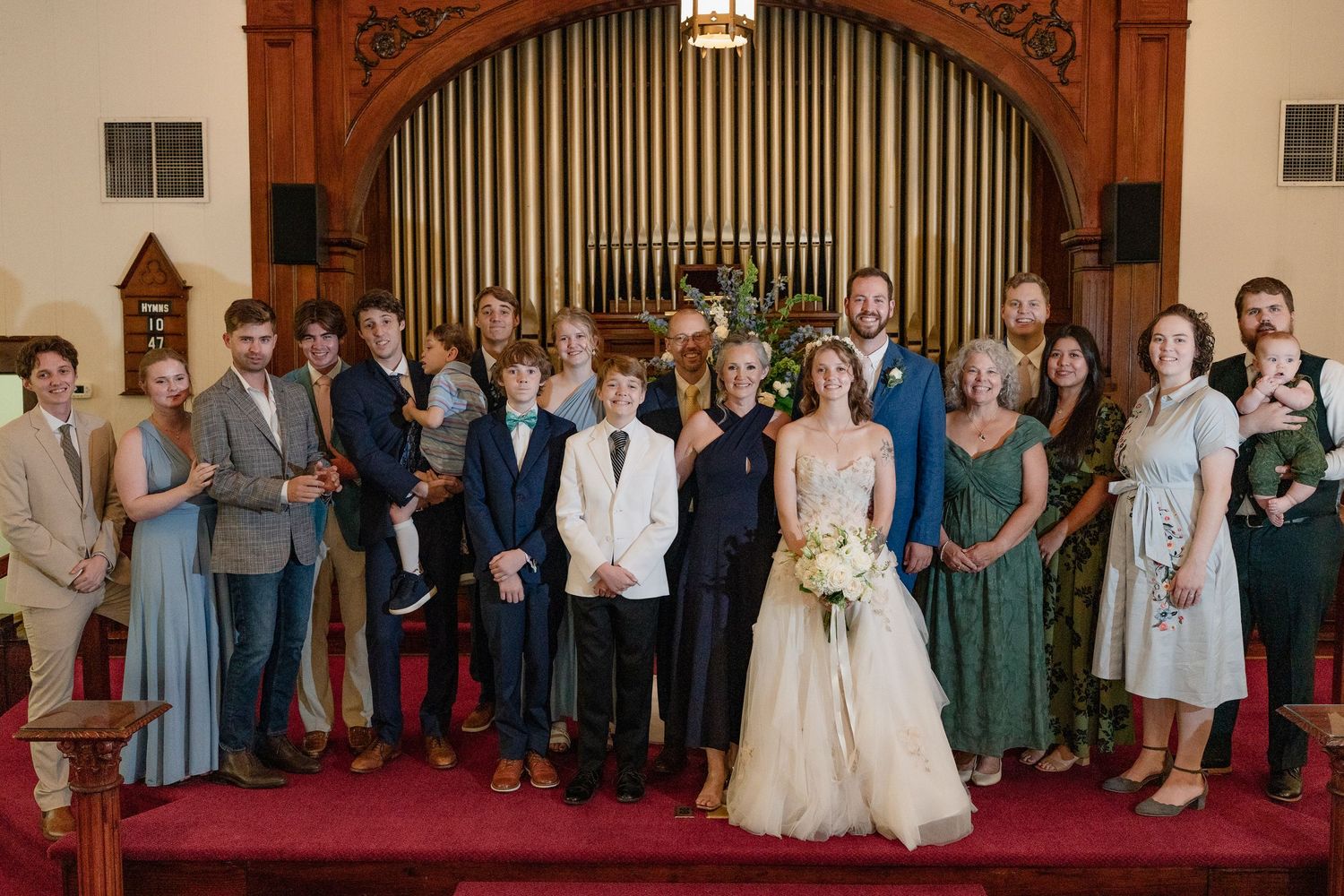 Wedding party and guests lined up in front of a church organ for a formal panoramic photograph.