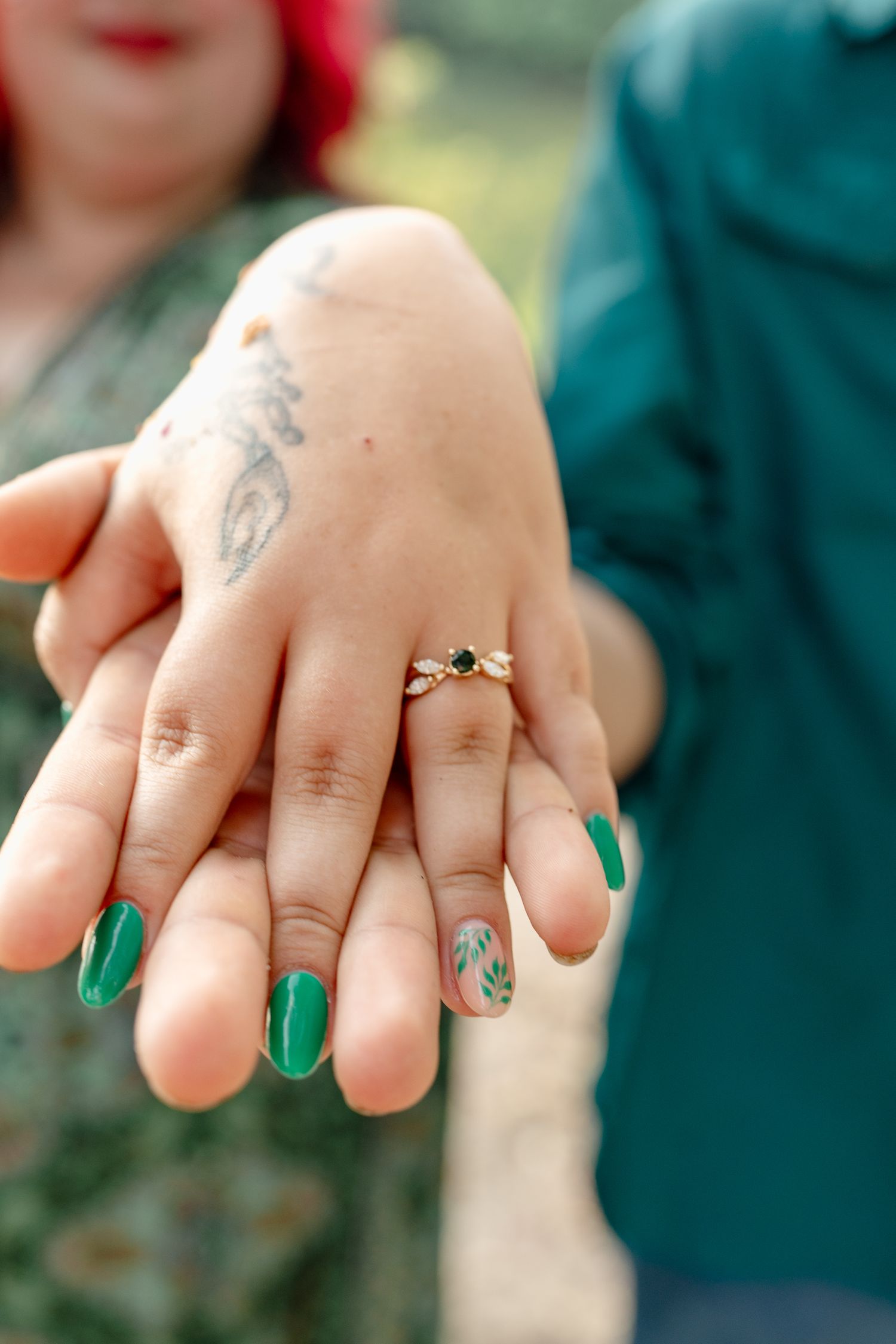 Close-up of hands with green nail polish and small tattoos showing off engagement rings.