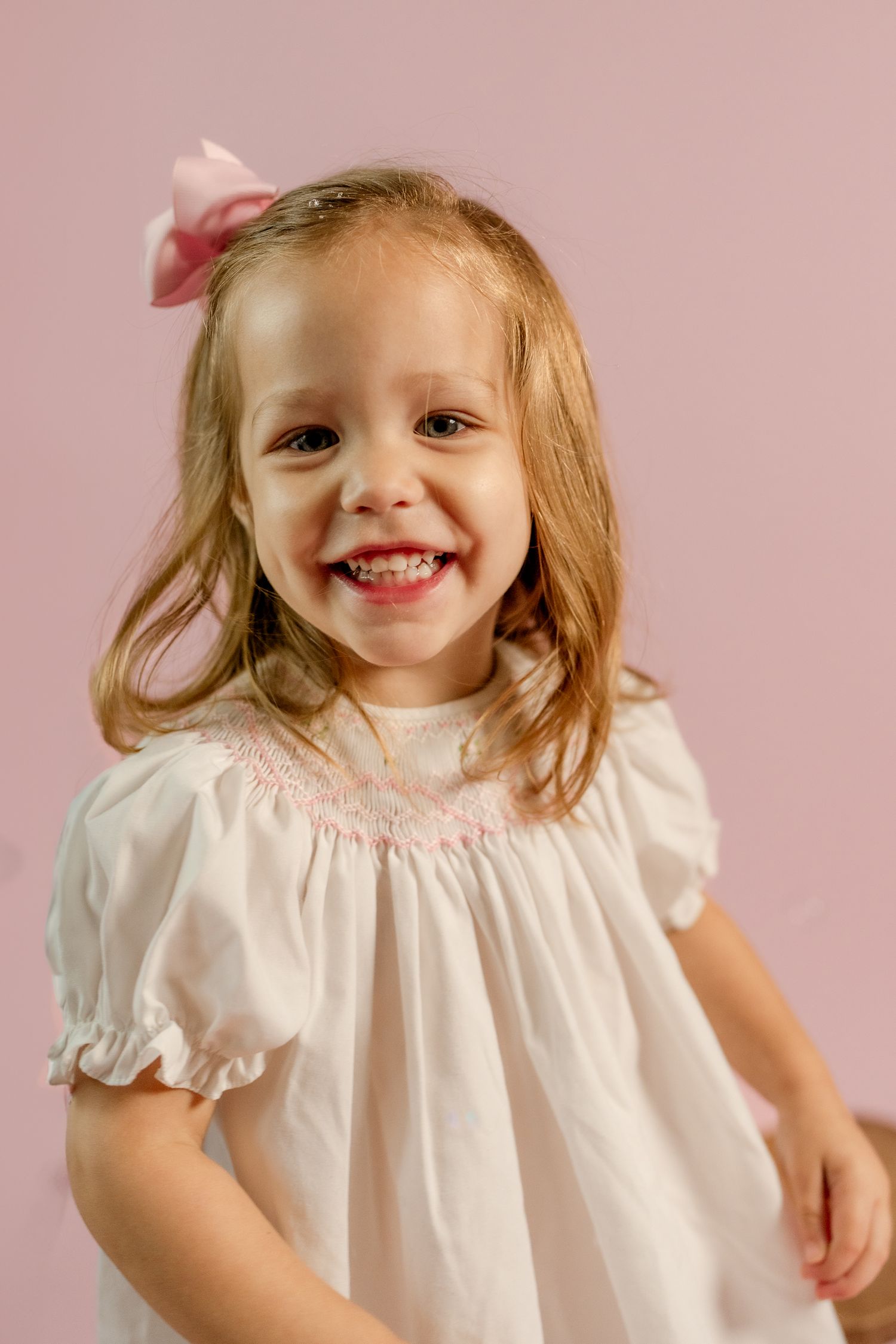 An adorable portrait showing pure joy against a soft pink background.