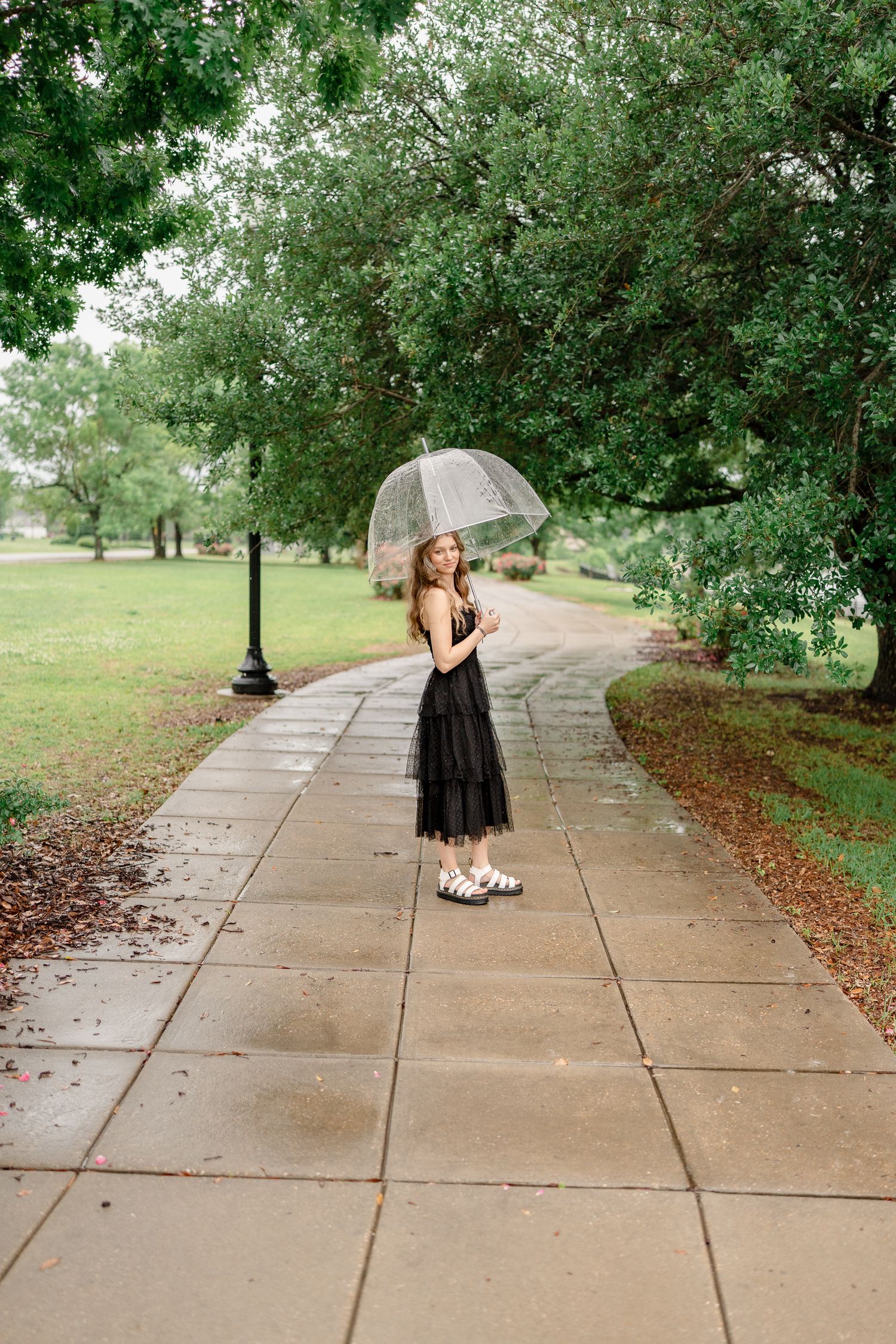 Fashion photography on tree-lined concrete path with grassy landscape.