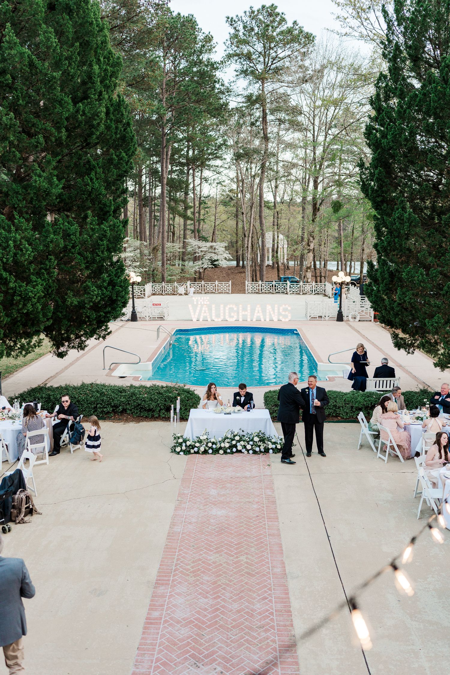 Wedding reception setup around a pool with string lights and elegant decor.