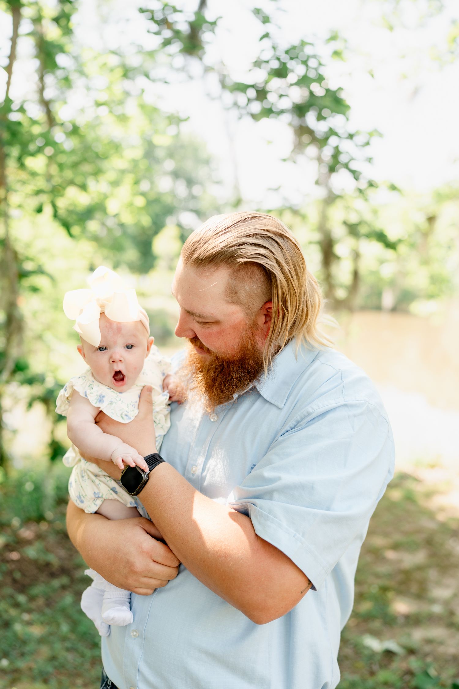 Playful interaction between parent and baby during outdoor photoshoot in a forest setting.