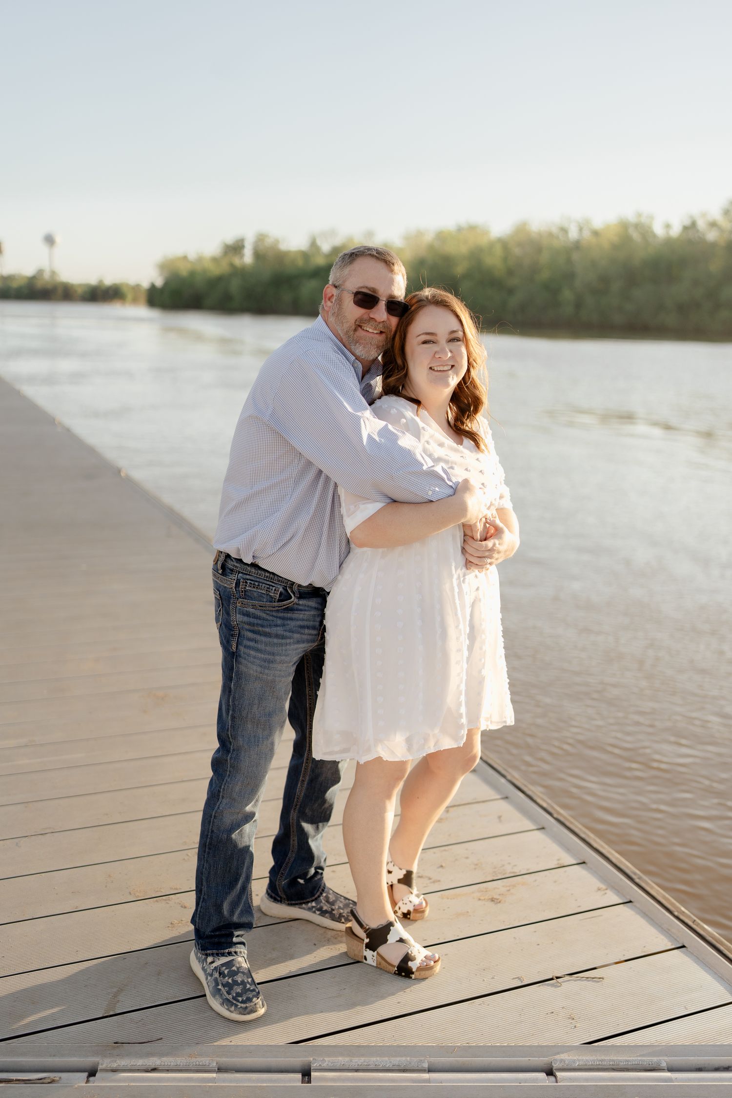 A couple poses for a portrait on a wooden pier during golden hour.