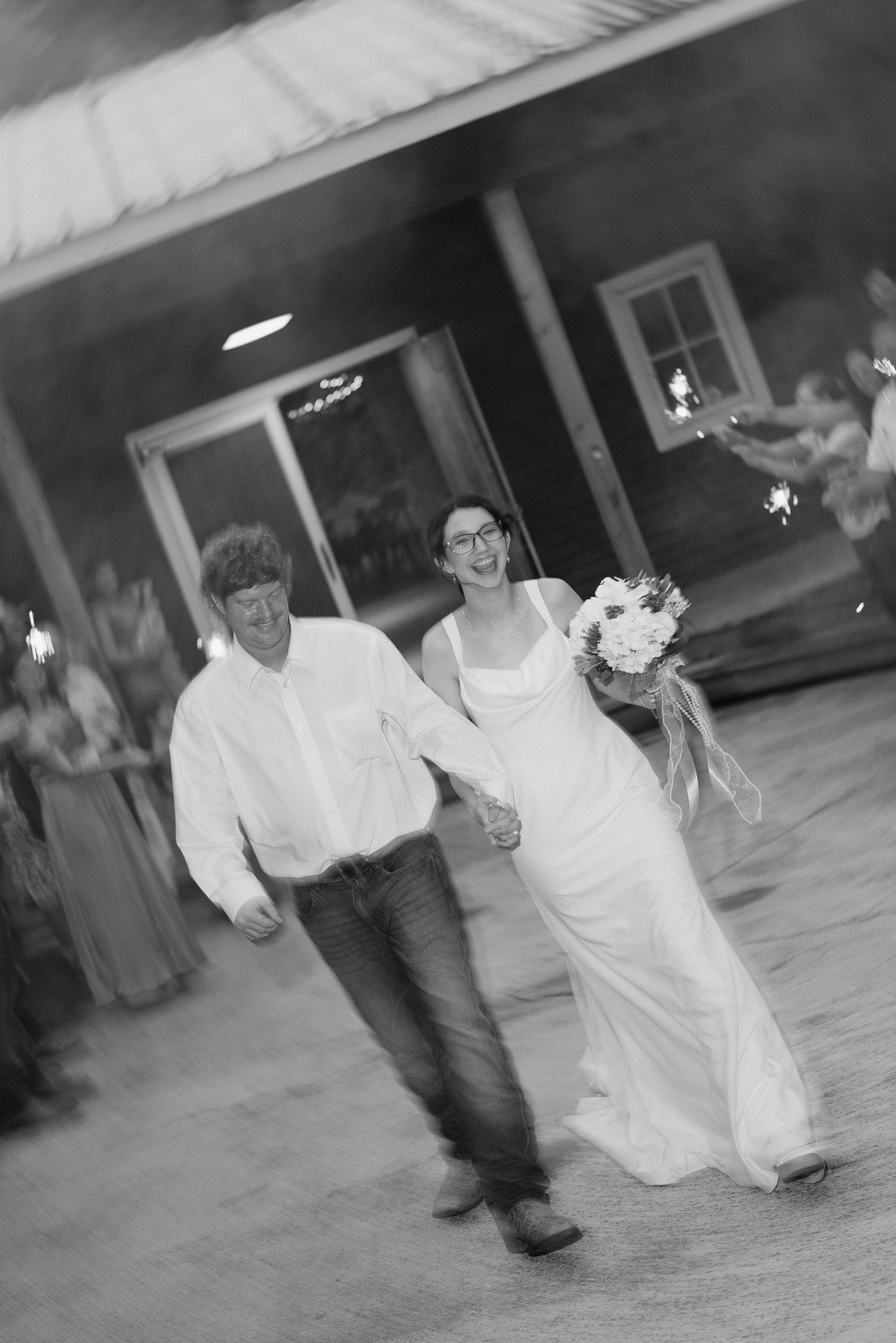 Black and white photo of newlyweds walking hand in hand amid sparklers after their rustic barn wedding.