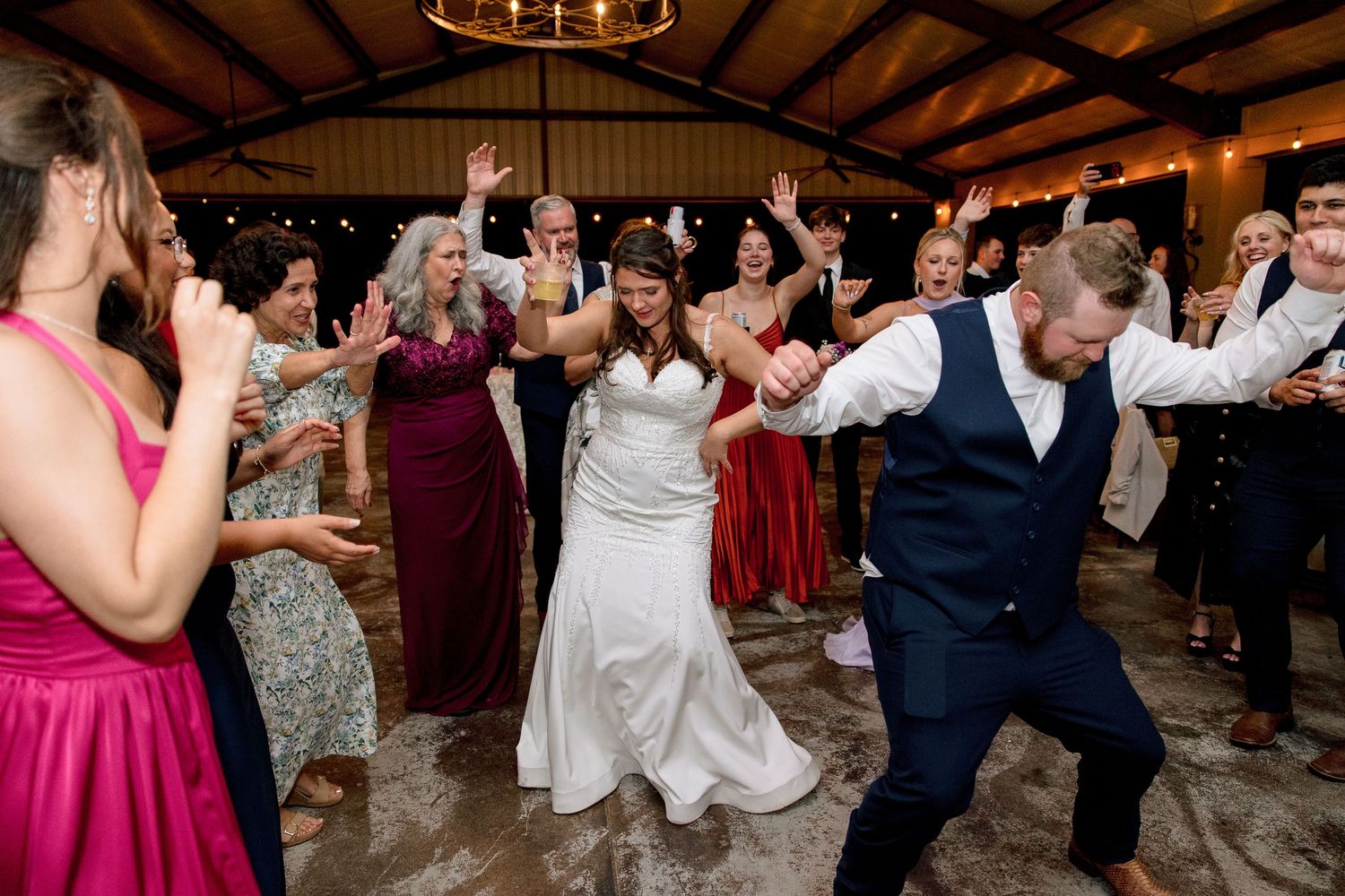 Bride and groom dancing joyfully with guests at lively indoor wedding reception celebration.