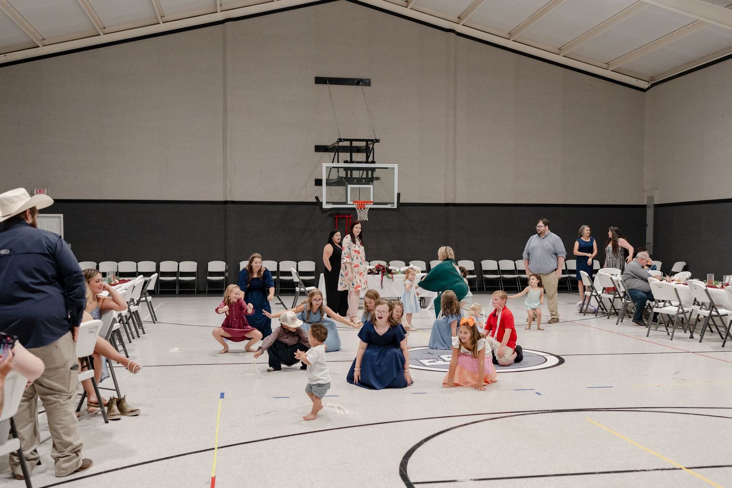 People gather in a gymnasium with chairs set up around the perimeter of a circular court during an indoor event.