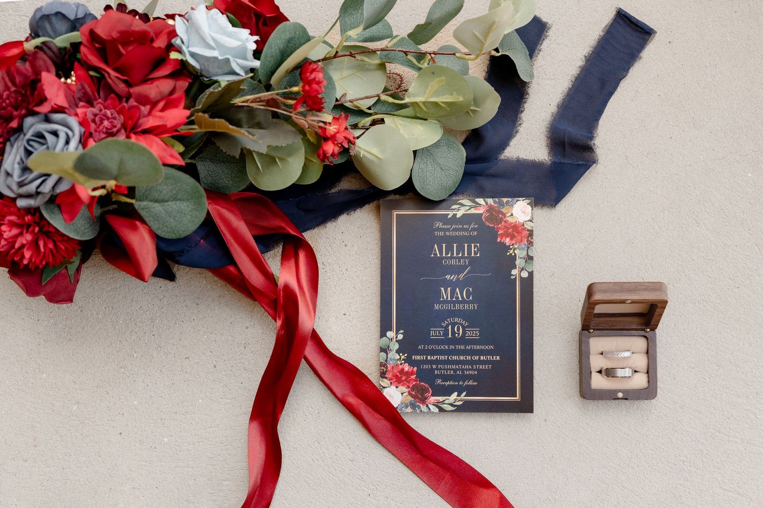 Wedding decor featuring red roses, eucalyptus leaves, and navy blue invitation cards.
