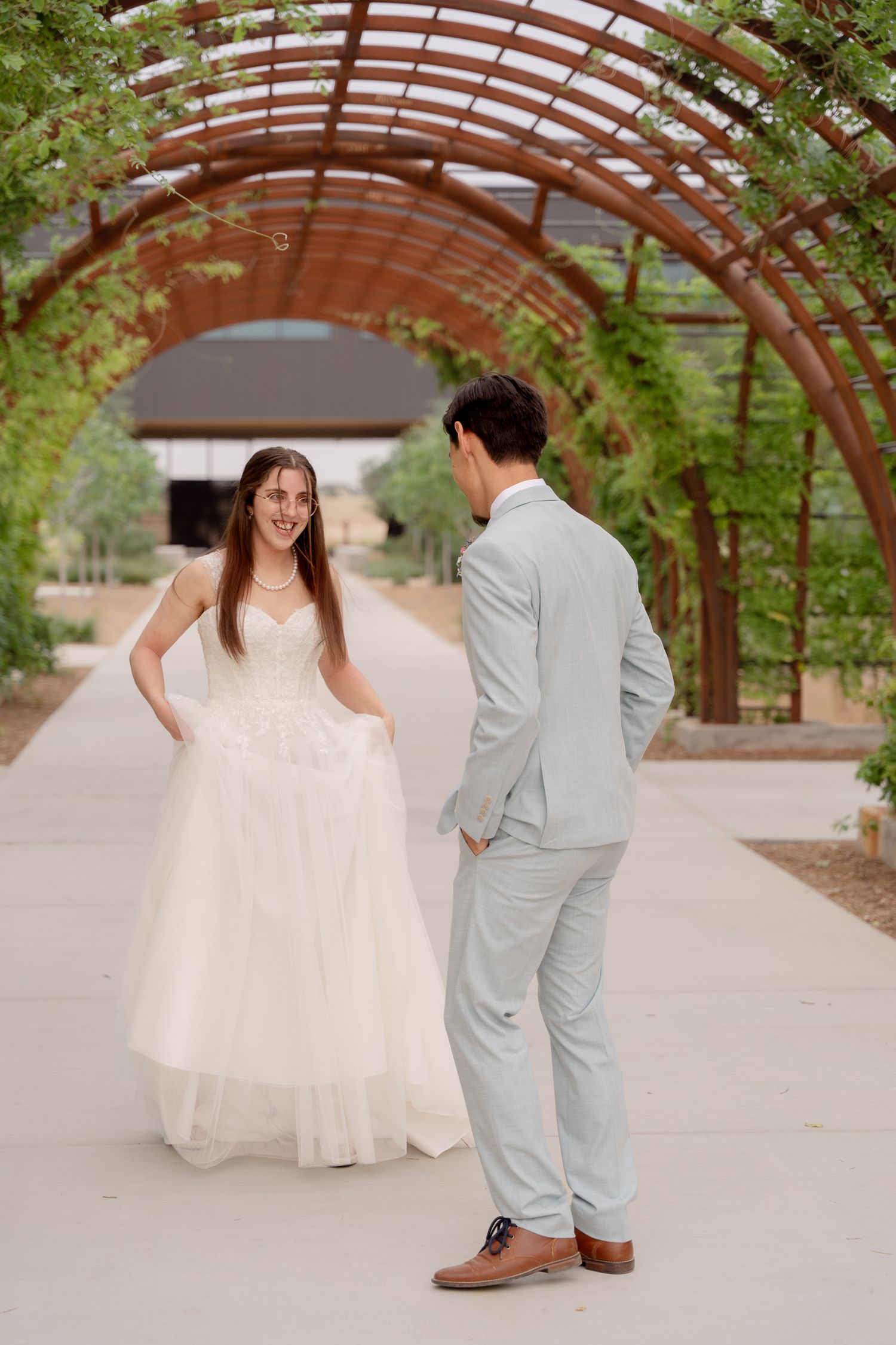 Bride and groom share playful moments during their first look under a rustic wooden archway.