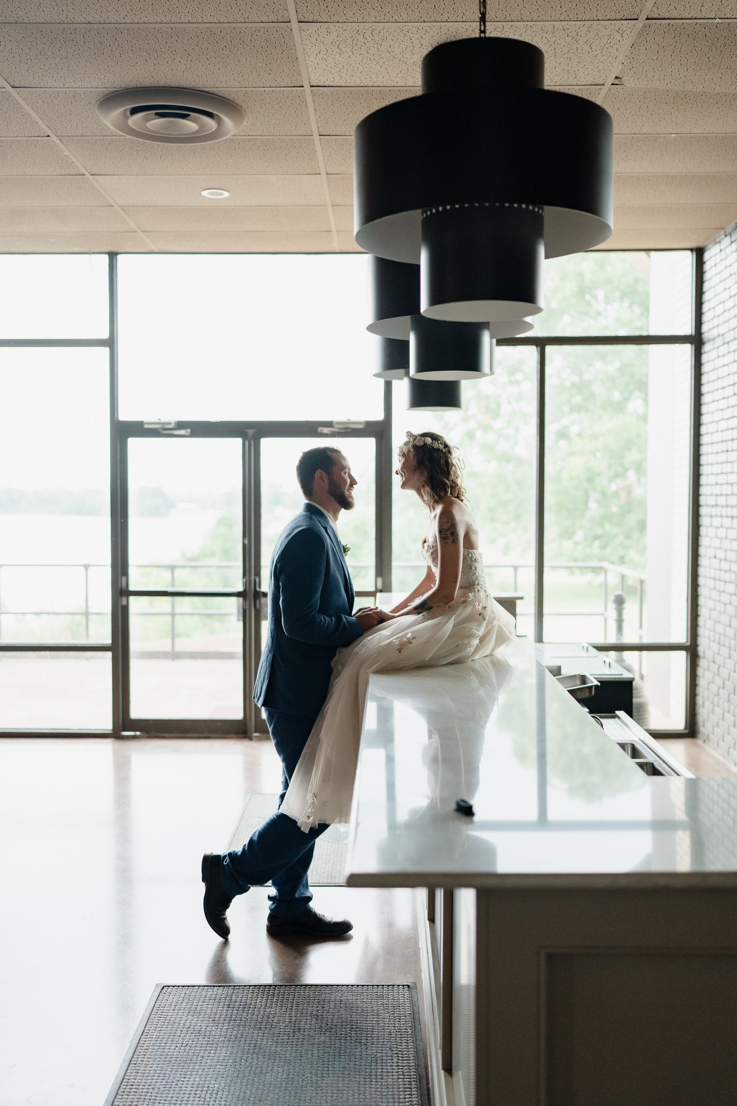 A couple shares an intimate moment in a modern room with large pendant lights and windows.