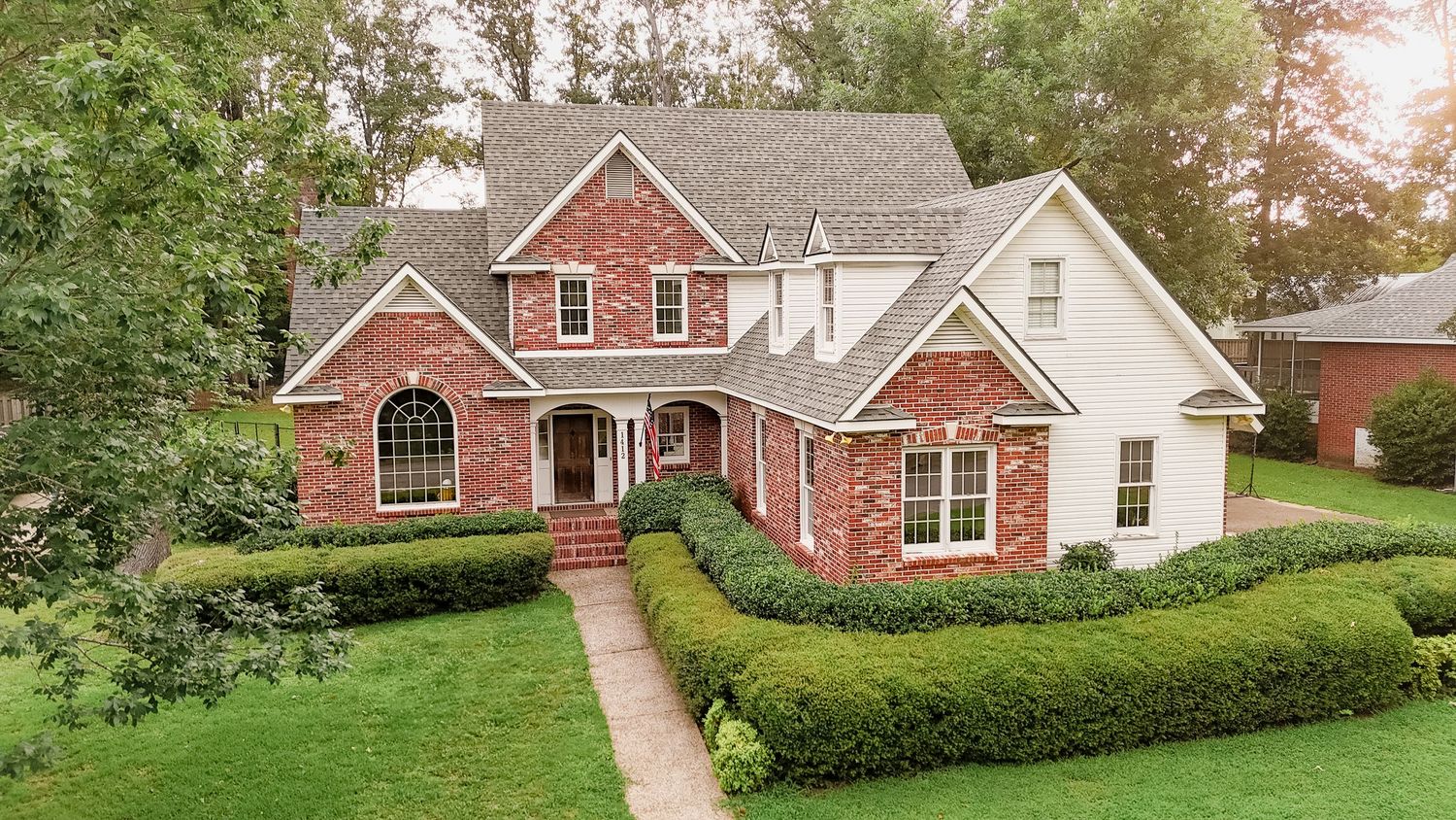 Aerial view of a red brick traditional two-story home with manicured hedges and landscaping on a lush green lawn.