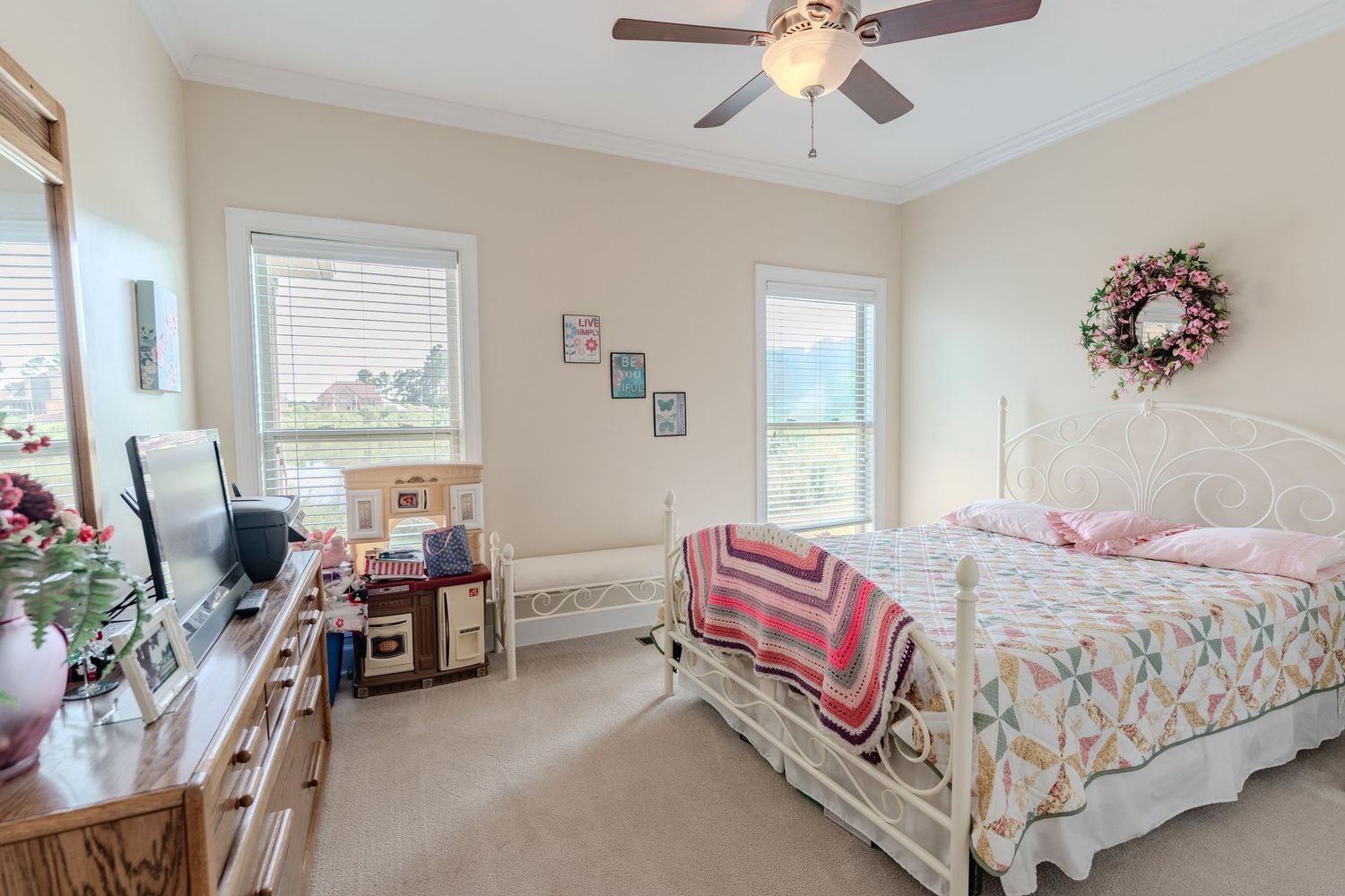 Panoramic view of a bright bedroom with beige walls, ceiling fan, and white furniture.