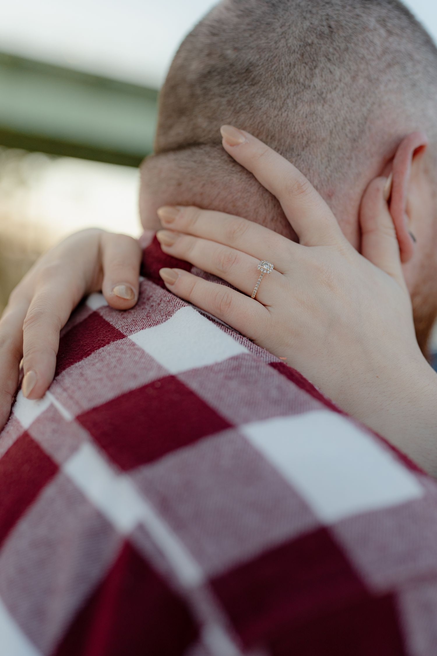 Close-up of hands with engagement rings resting on a red and white checkered blanket.