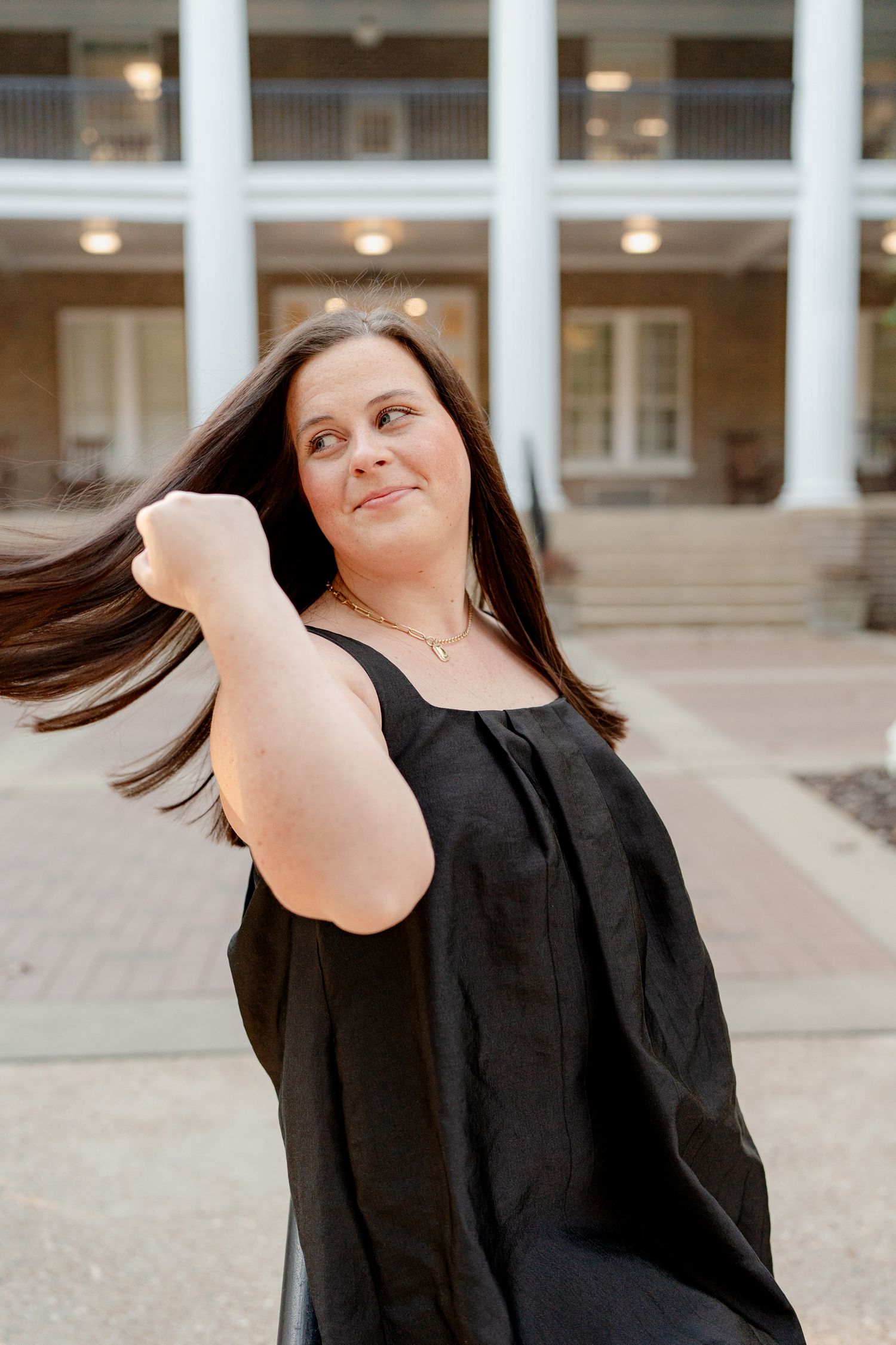 A series of dynamic hair flip photos showing movement and energy in a black outfit against a light architectural backdrop.