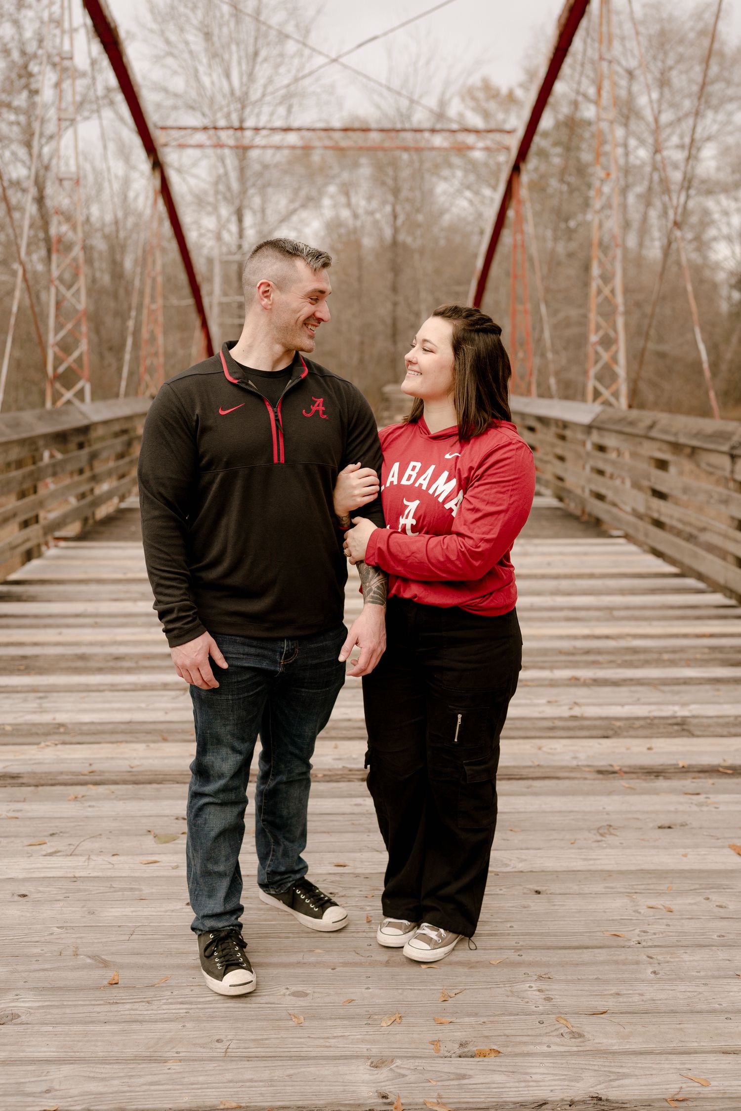 A couple shares a loving moment on a wooden bridge with red metal supports on an autumn day.