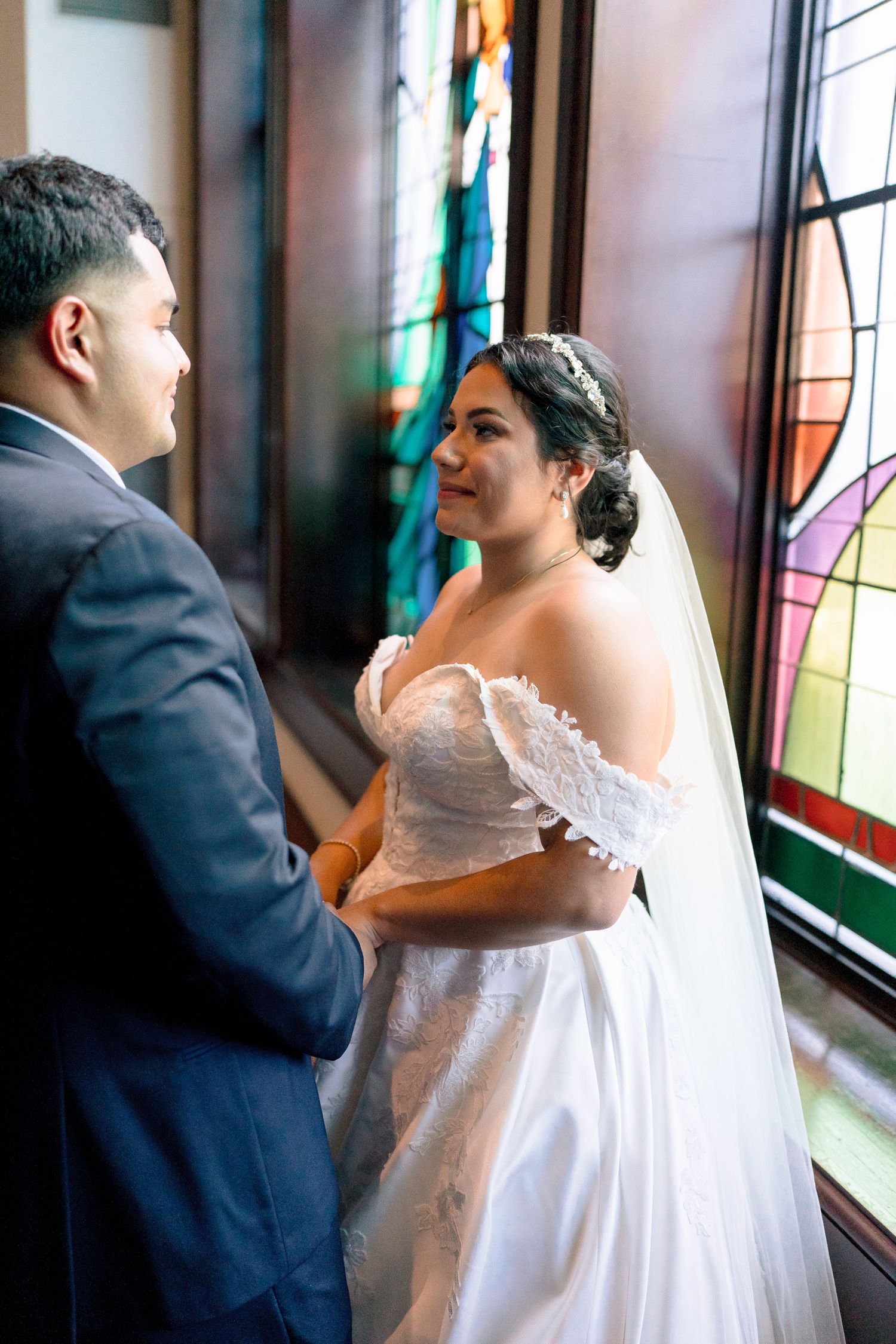 A romantic wedding couple shares an intimate moment near a stained glass window in a church.