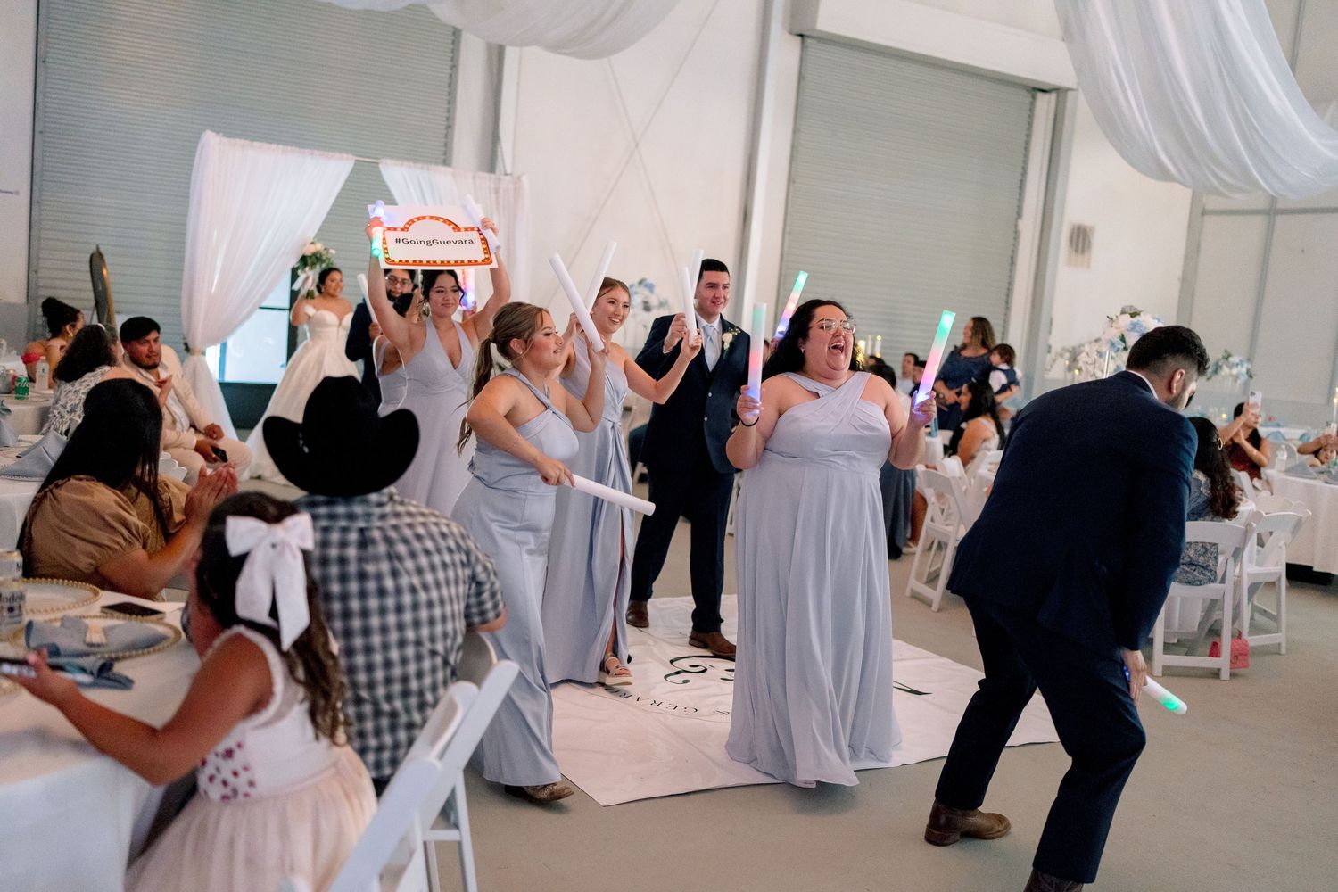 Wedding guests dance together in an elegant white reception venue during a celebration.