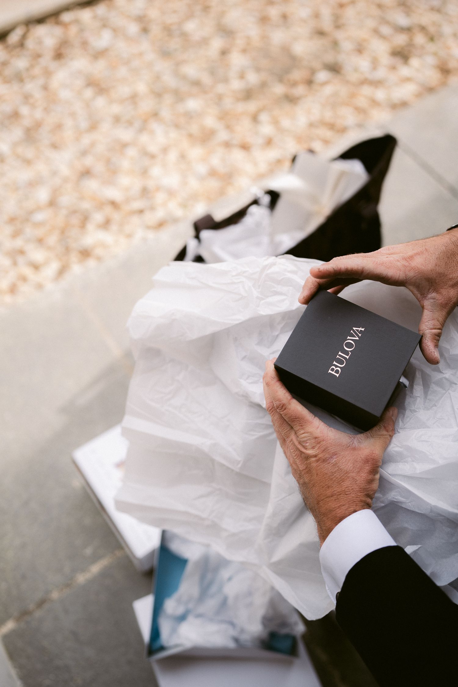 Hands carefully unwrap tissue paper revealing a black gift box at a formal event.
