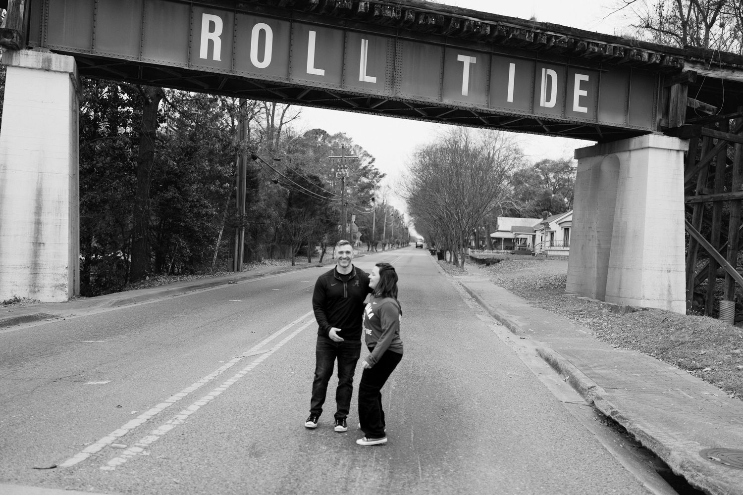 Two figures walk beneath a large bridge or overpass structure on an empty road.