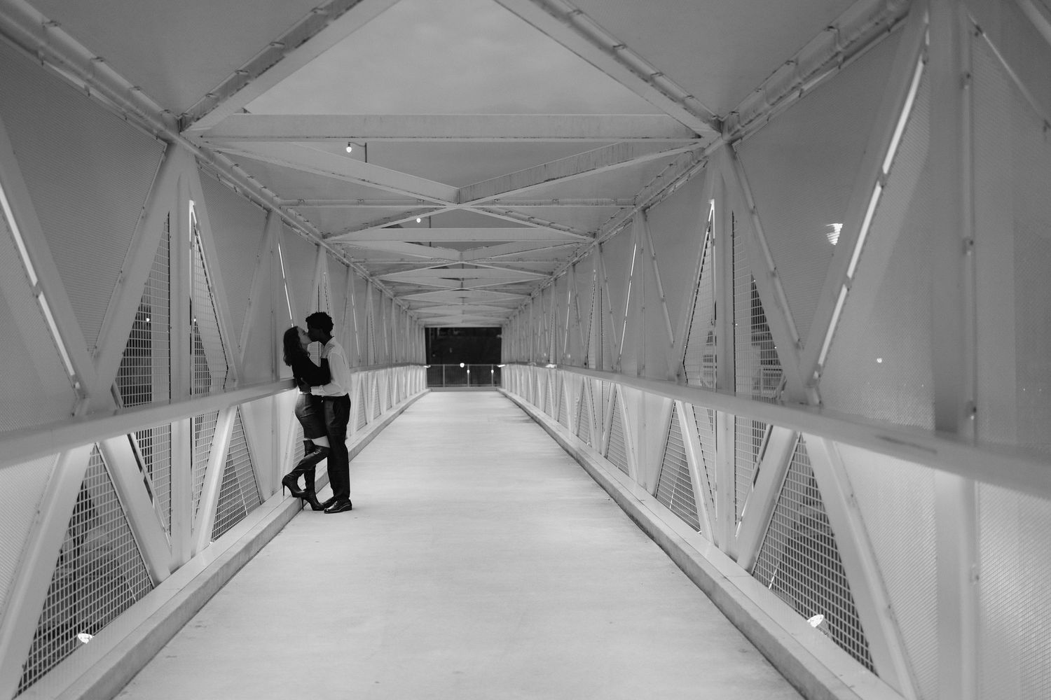A black and white photo of a couple sharing an intimate embrace inside a long illuminated bridge tunnel.