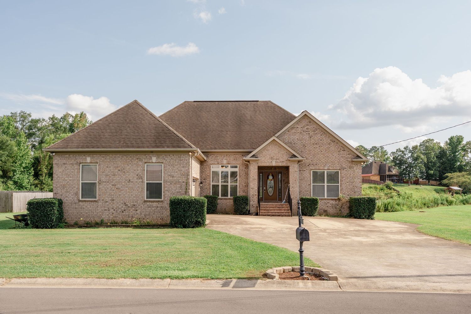 Large brick ranch-style home with tan siding and brown roof set against a cloudy sky and green lawn.
