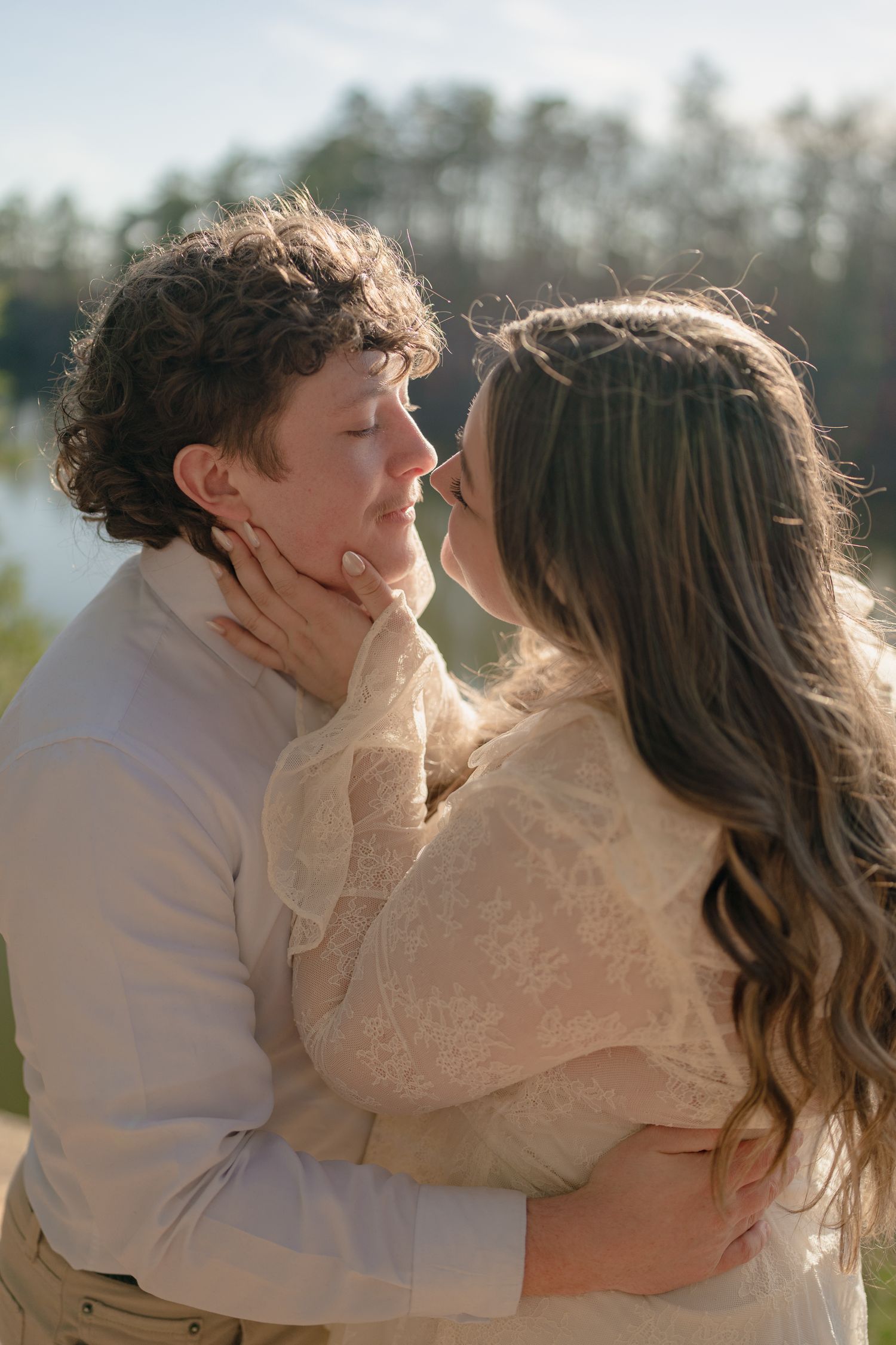 Couple sharing a tender moment, woman cradling man's face as they lean in for a kiss outdoors.