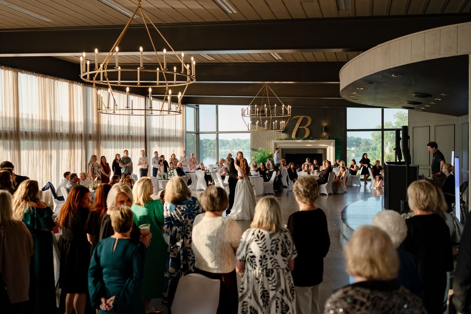 Large group celebrates at an elegant event space with chandeliers and floor-to-ceiling windows.