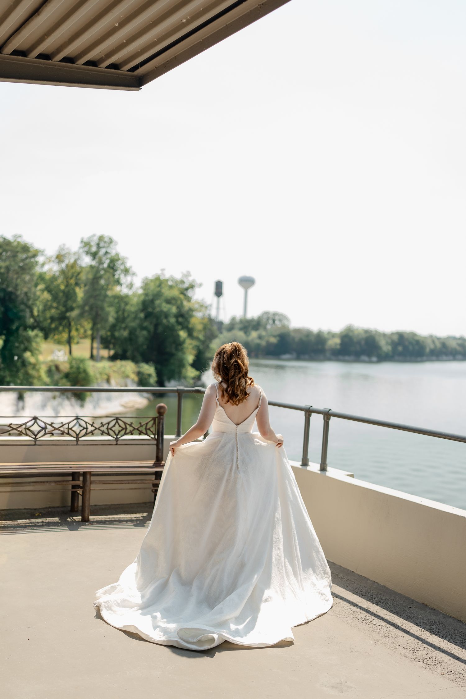 White wedding dress flowing in the breeze on a lakeside balcony with scenic water views.