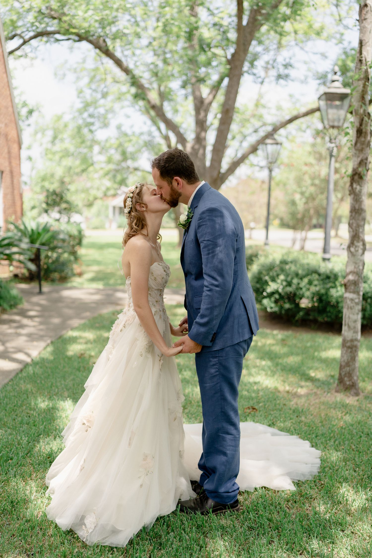 A romantic wedding couple shares tender moments in a lush garden setting with trees and greenery.