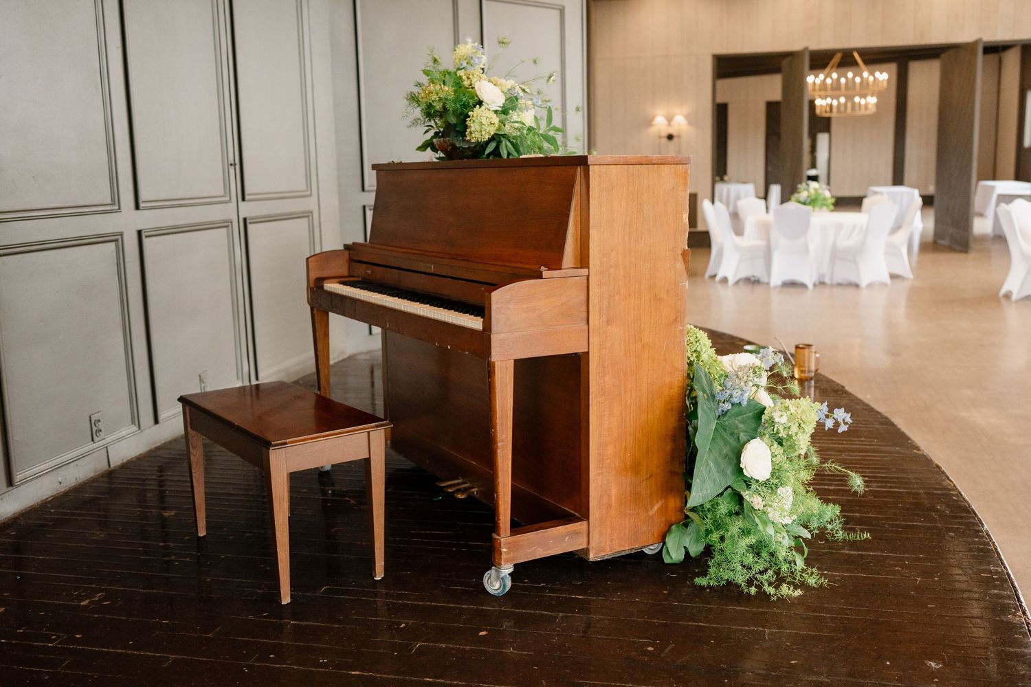 Upright piano adorned with cascading white floral arrangements in an elegant event space.