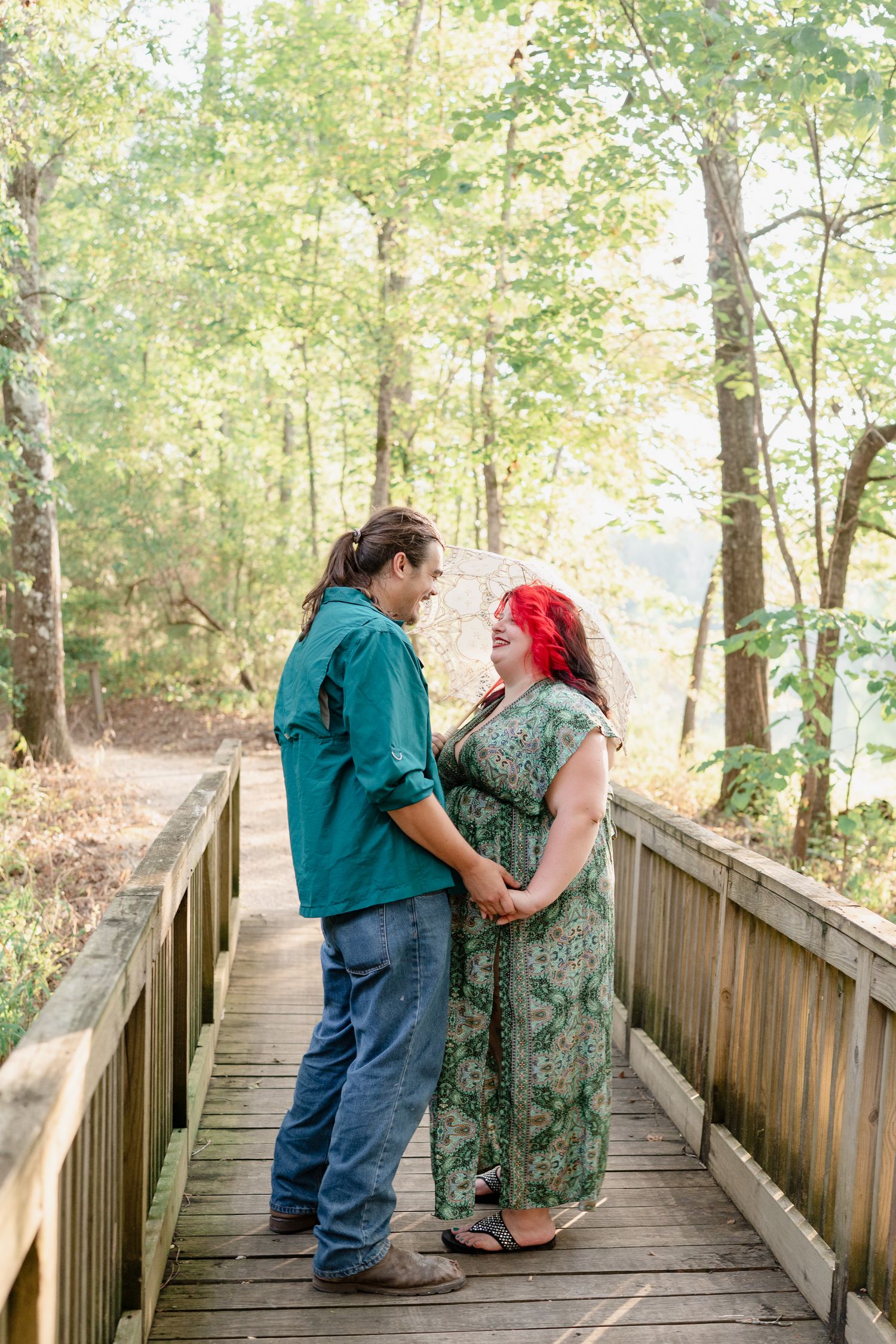 A couple stands together on a wooden boardwalk surrounded by lush green forest on a sunny afternoon.