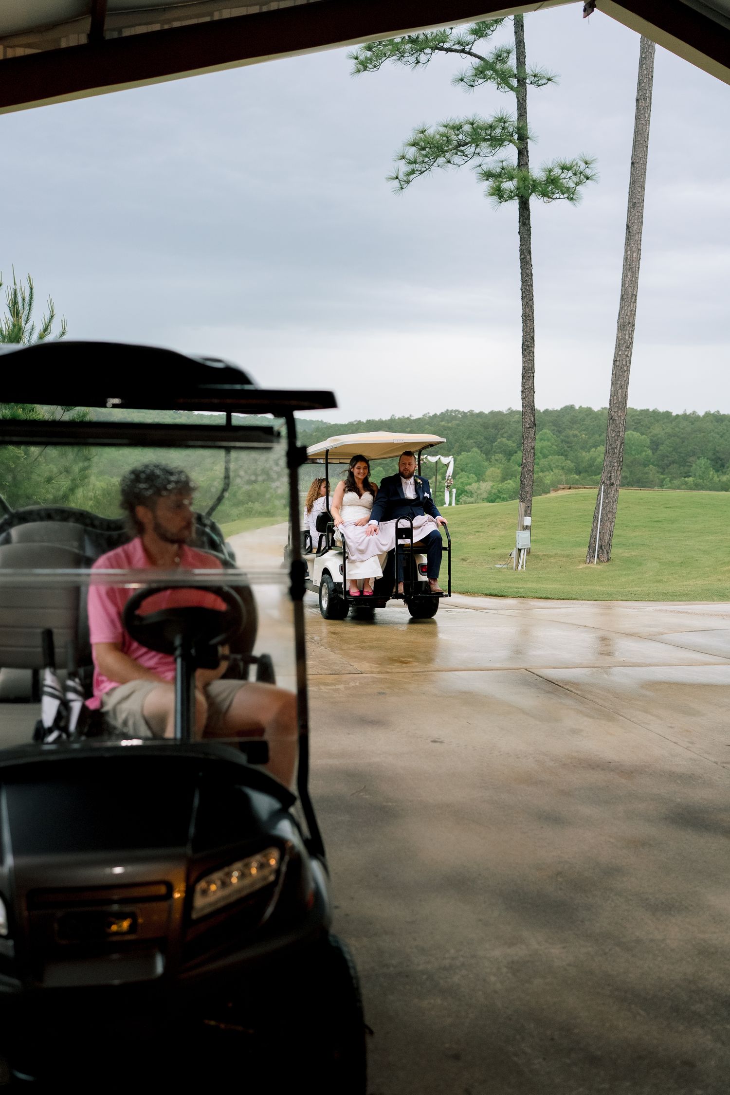 Wedding party riding golf carts on a rainy day at a golf course, with tall pine trees in the background.