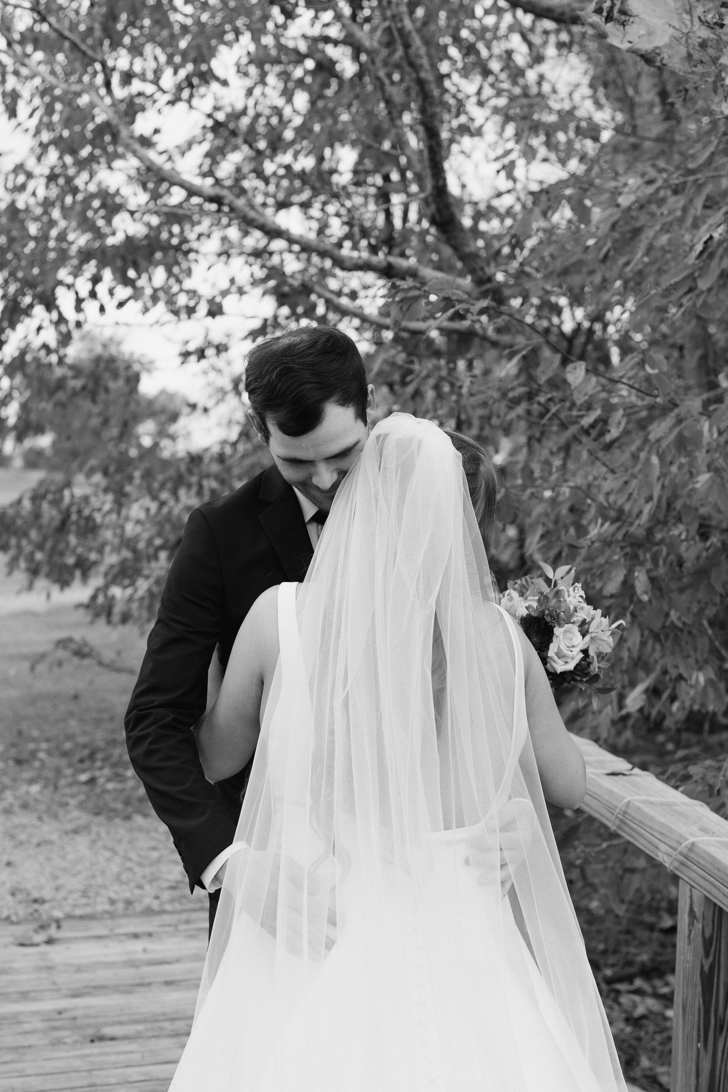 A romantic black and white photo series shows a couple in wedding attire sharing intimate moments on a wooden deck outdoors.