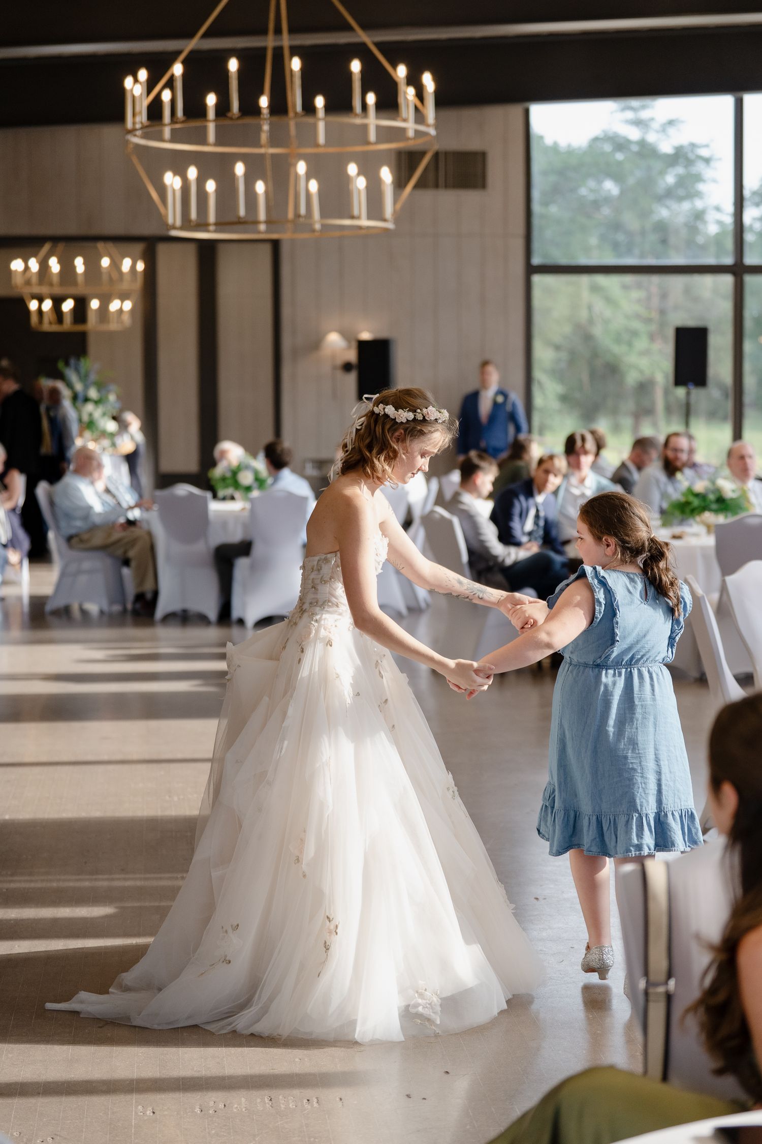 Wedding reception dance floor scene with guests in formal attire under elegant chandeliers.