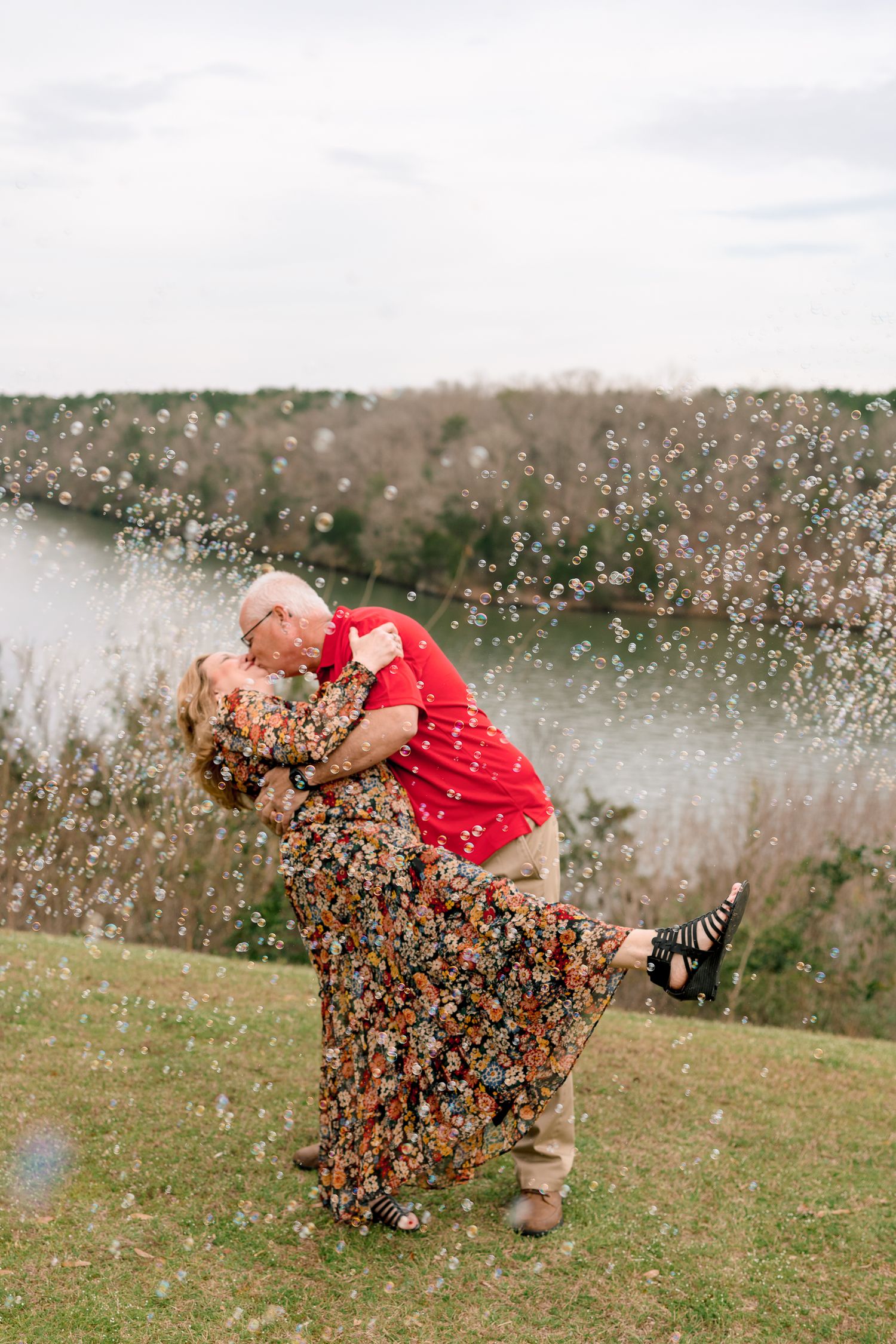 Couple sharing a romantic dip kiss surrounded by bubbles with a river in the background.