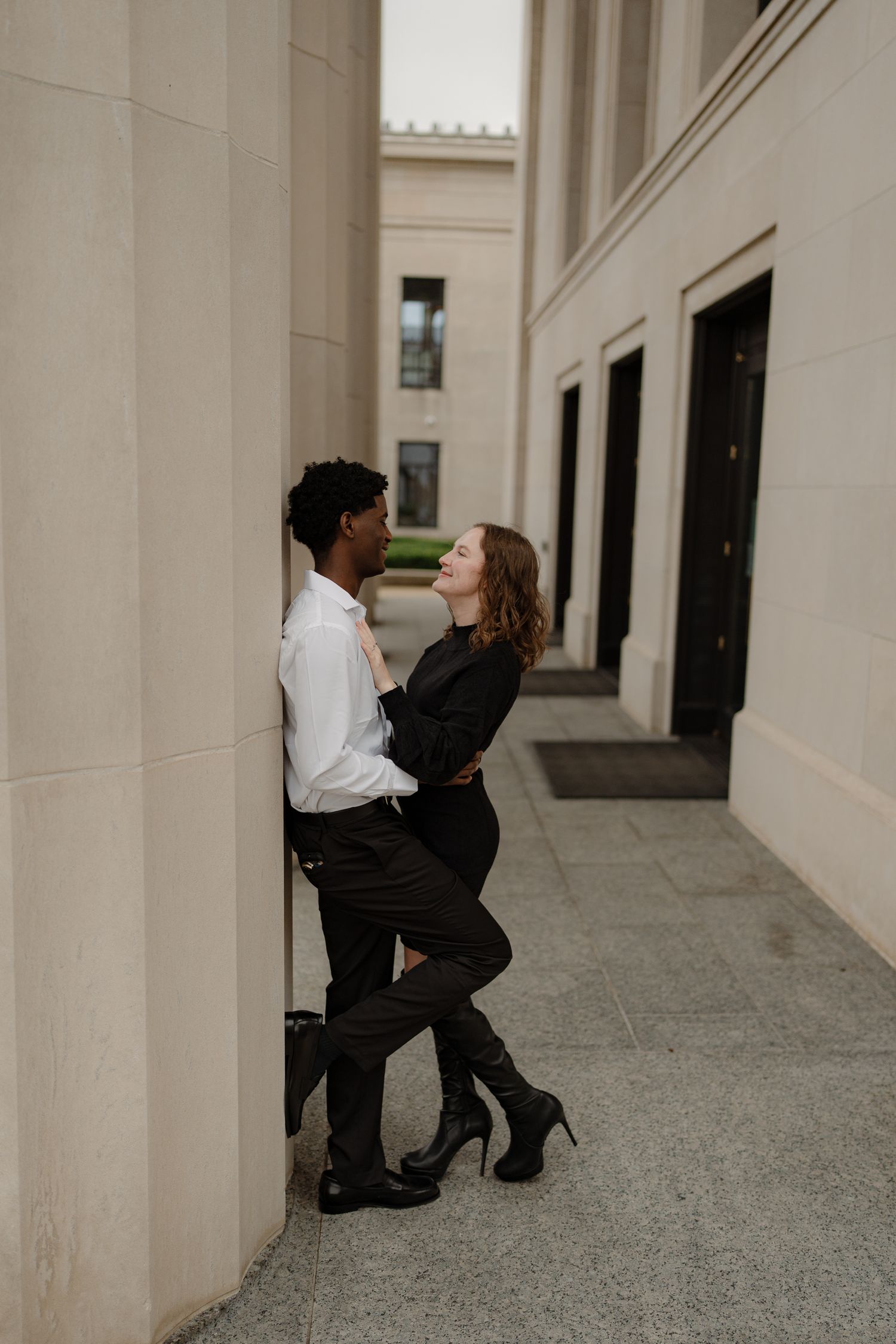 Interracial couple sharing an intimate moment leaning against stone columns of a grand building.