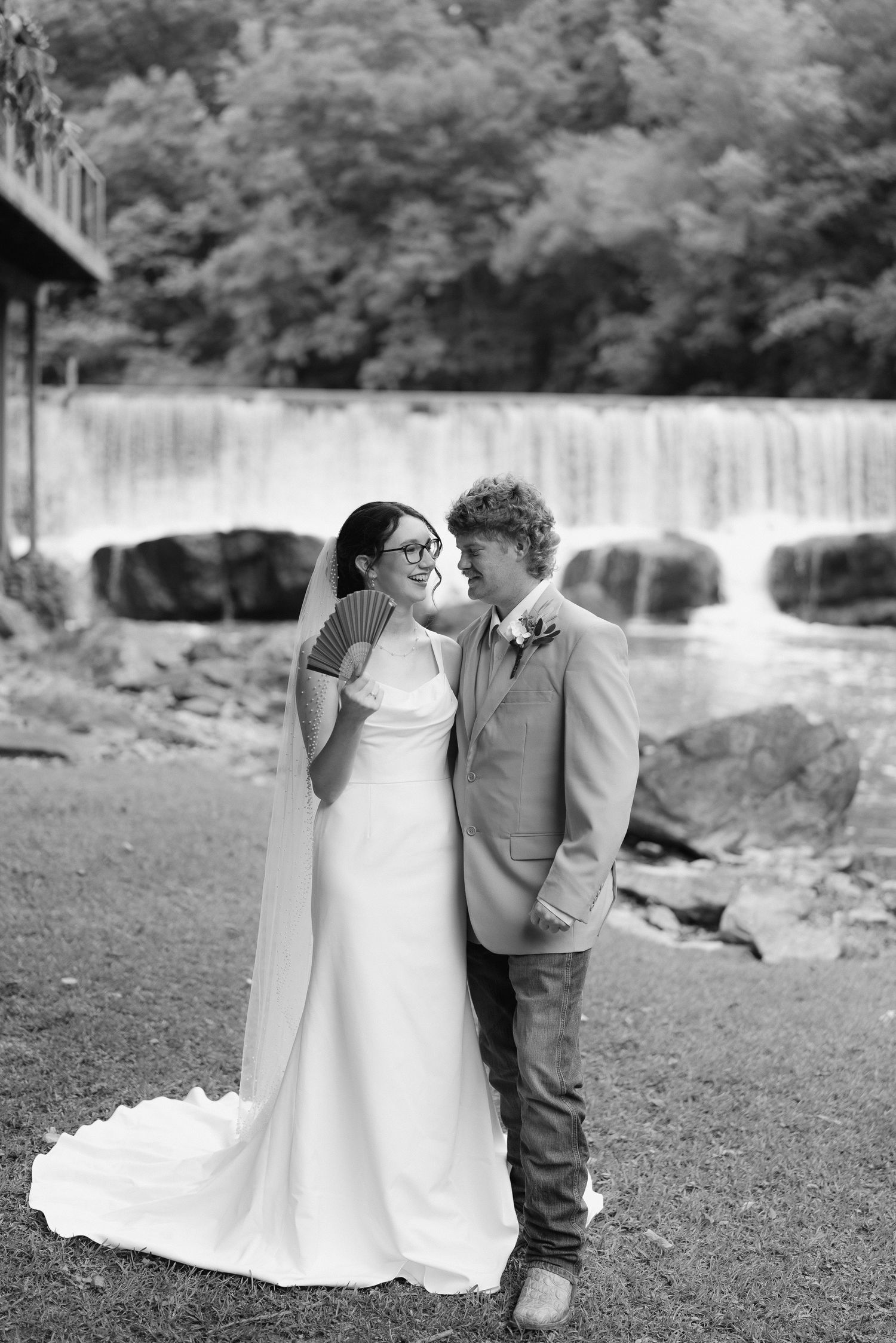 Black and white photo of bride and groom smiling together near a waterfall and stone bridge.
