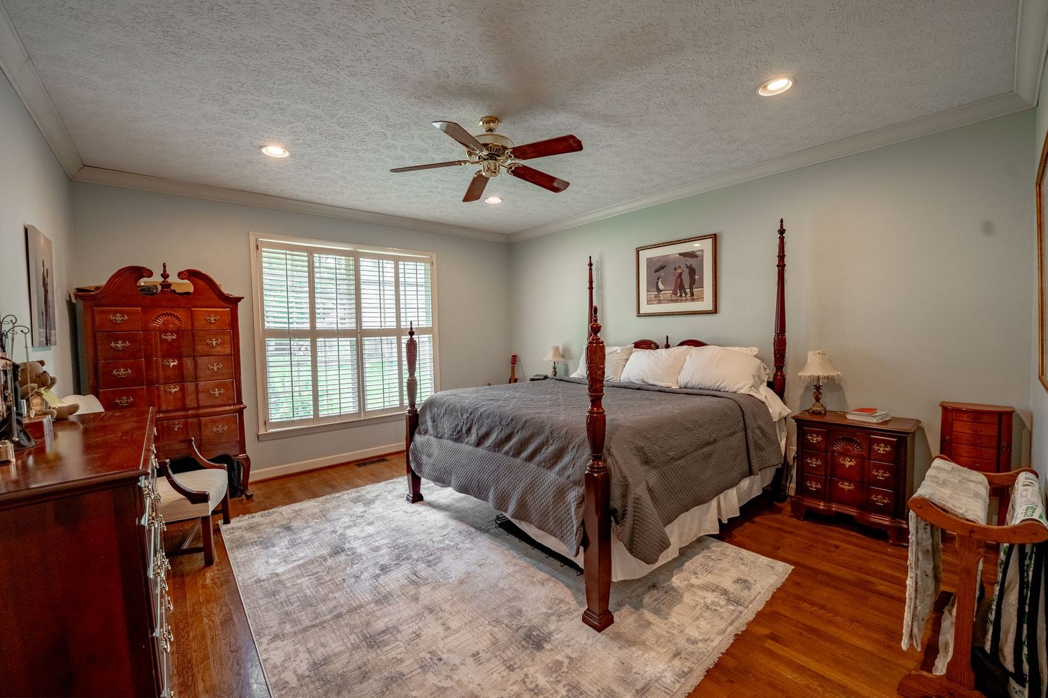 Spacious master bedroom with four-poster bed, hardwood floors, ceiling fan and antique wooden furniture.