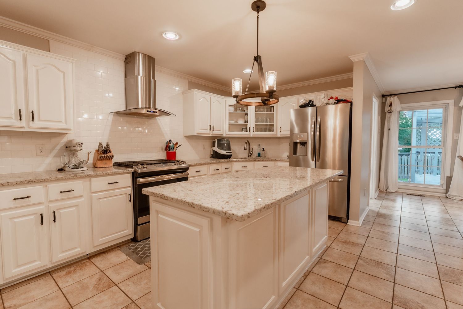 Modern white kitchen with quartz countertops, stainless steel appliances, and pendant lighting in an open concept layout.
