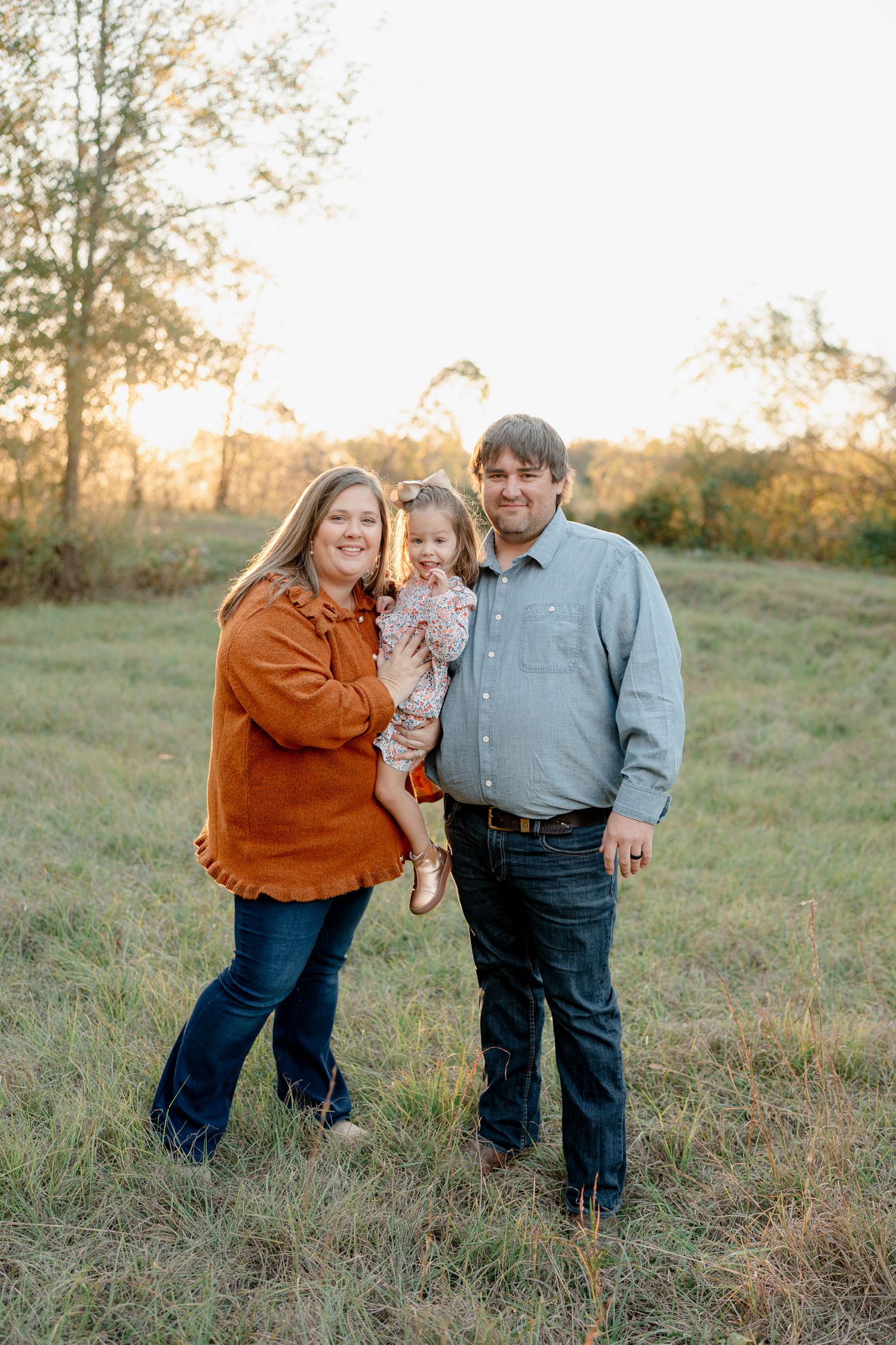A family shares joyful moments together in a sunlit grassy field during golden hour.