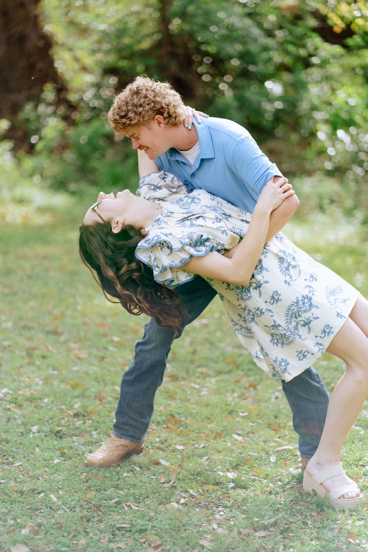 A couple shares a fun dip-style dance move in a grassy outdoor setting.