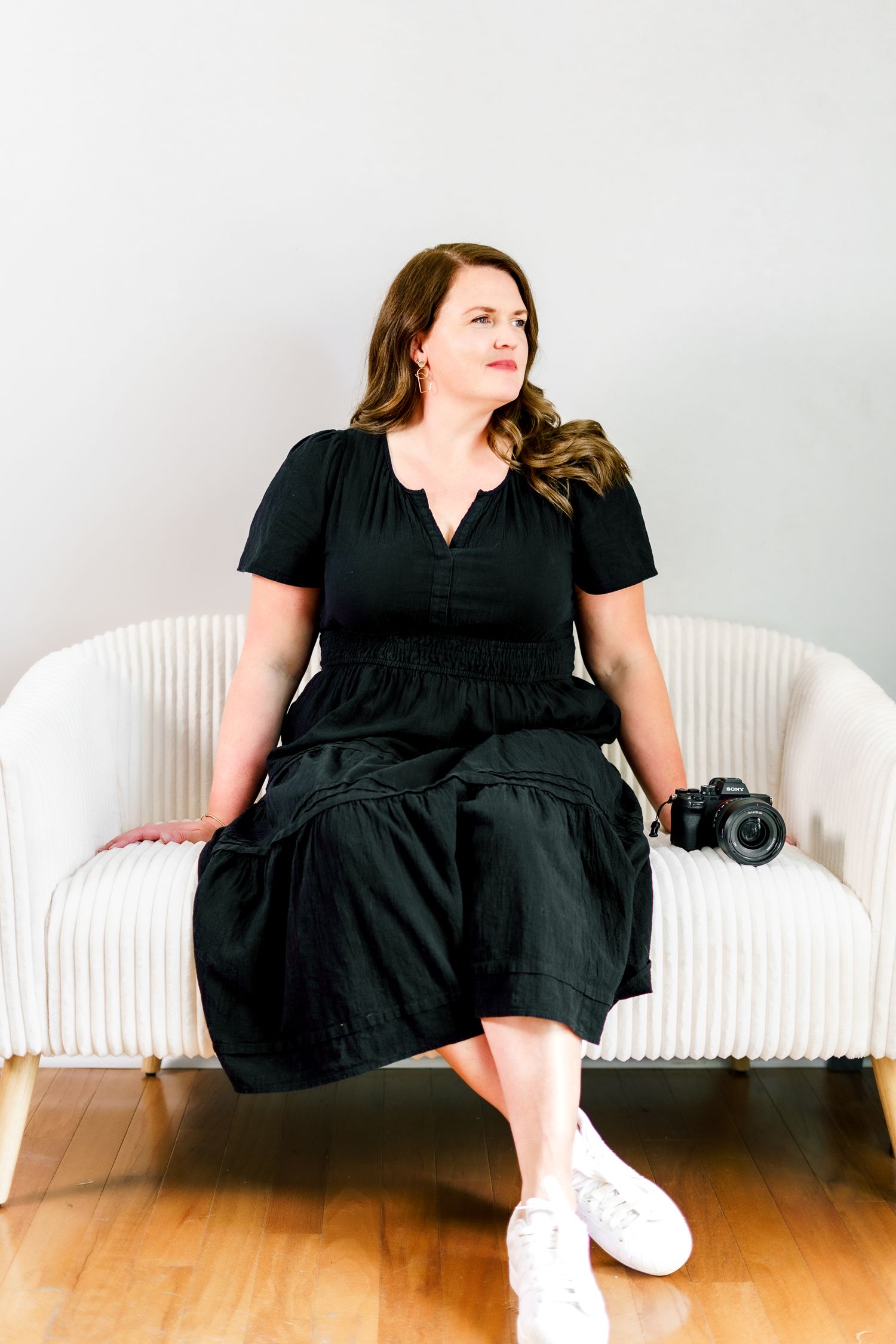 A person in a black dress sits casually on a white modern bench during a photo session.