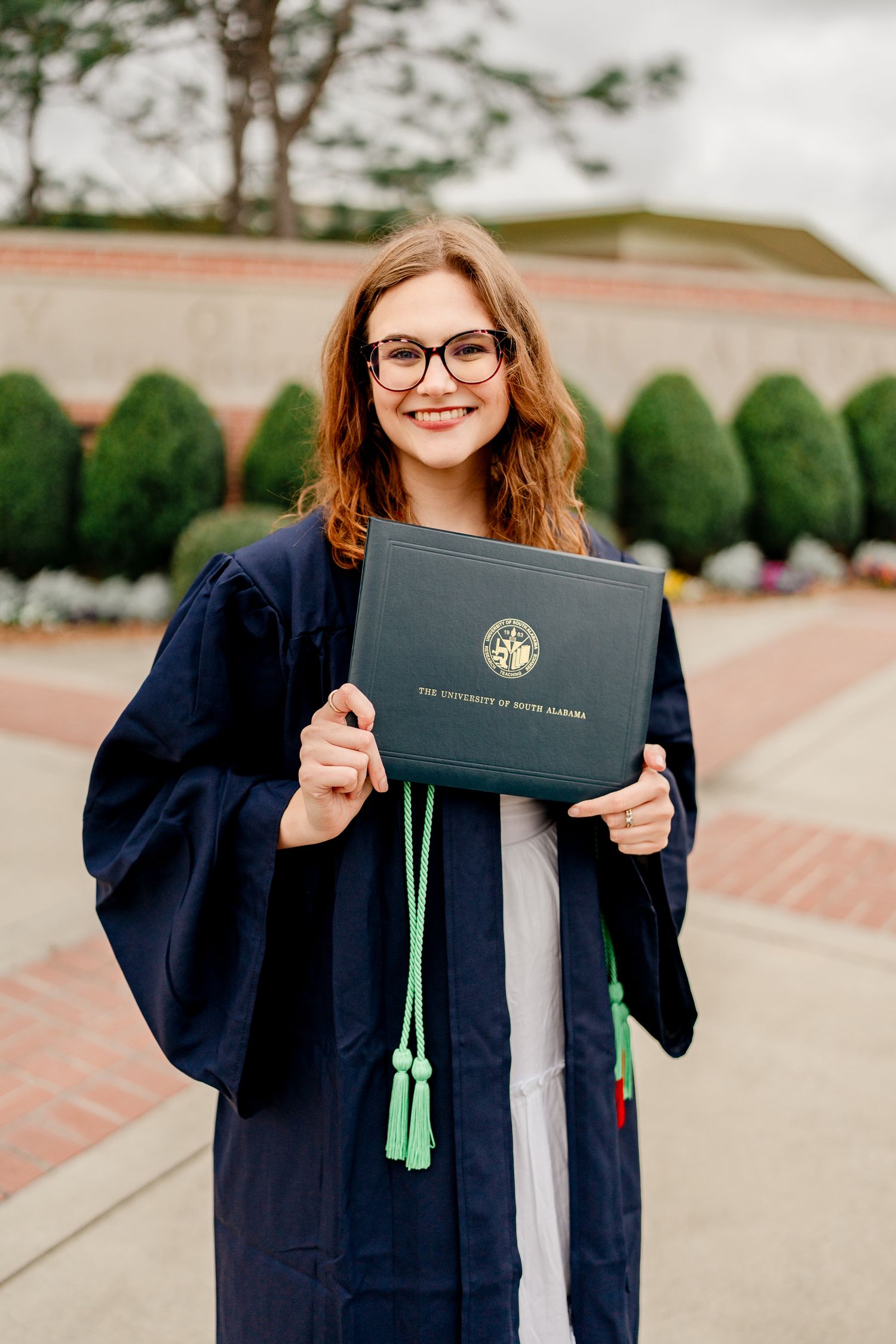 Graduate proudly displaying diploma holder in navy graduation gown.