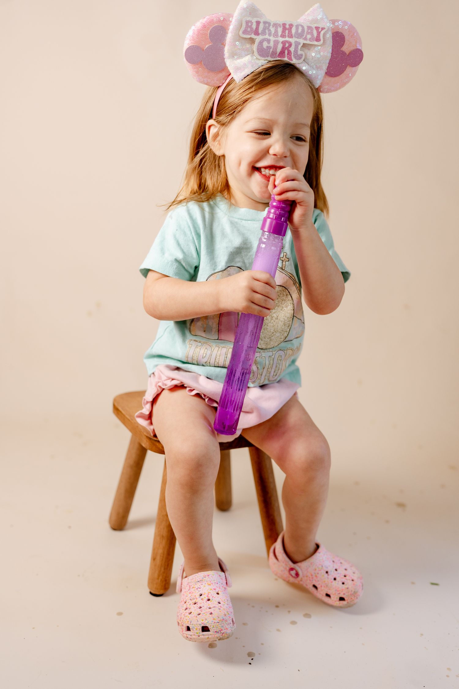 A wooden stool and purple bubble wand are arranged against a cream colored background.