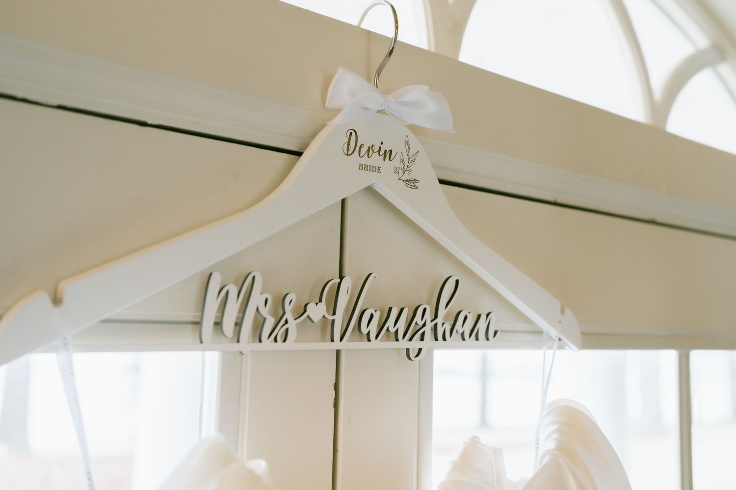Custom white wooden wedding hanger with personalized name displayed near window.