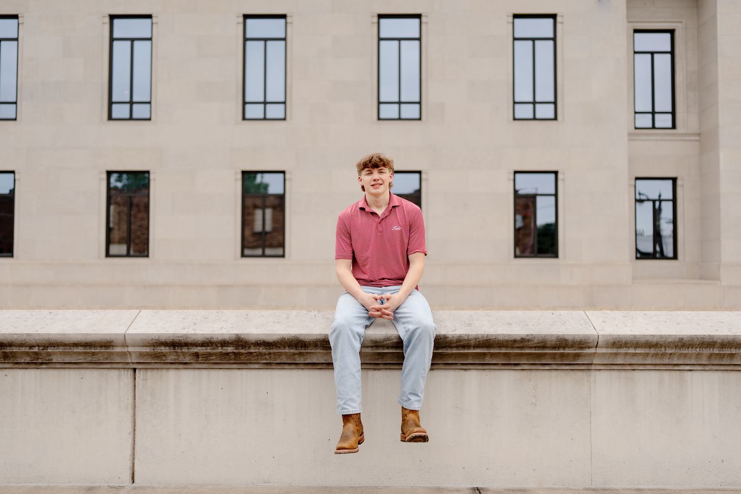 A beige building facade with multiple windows and someone sitting on the ledge.