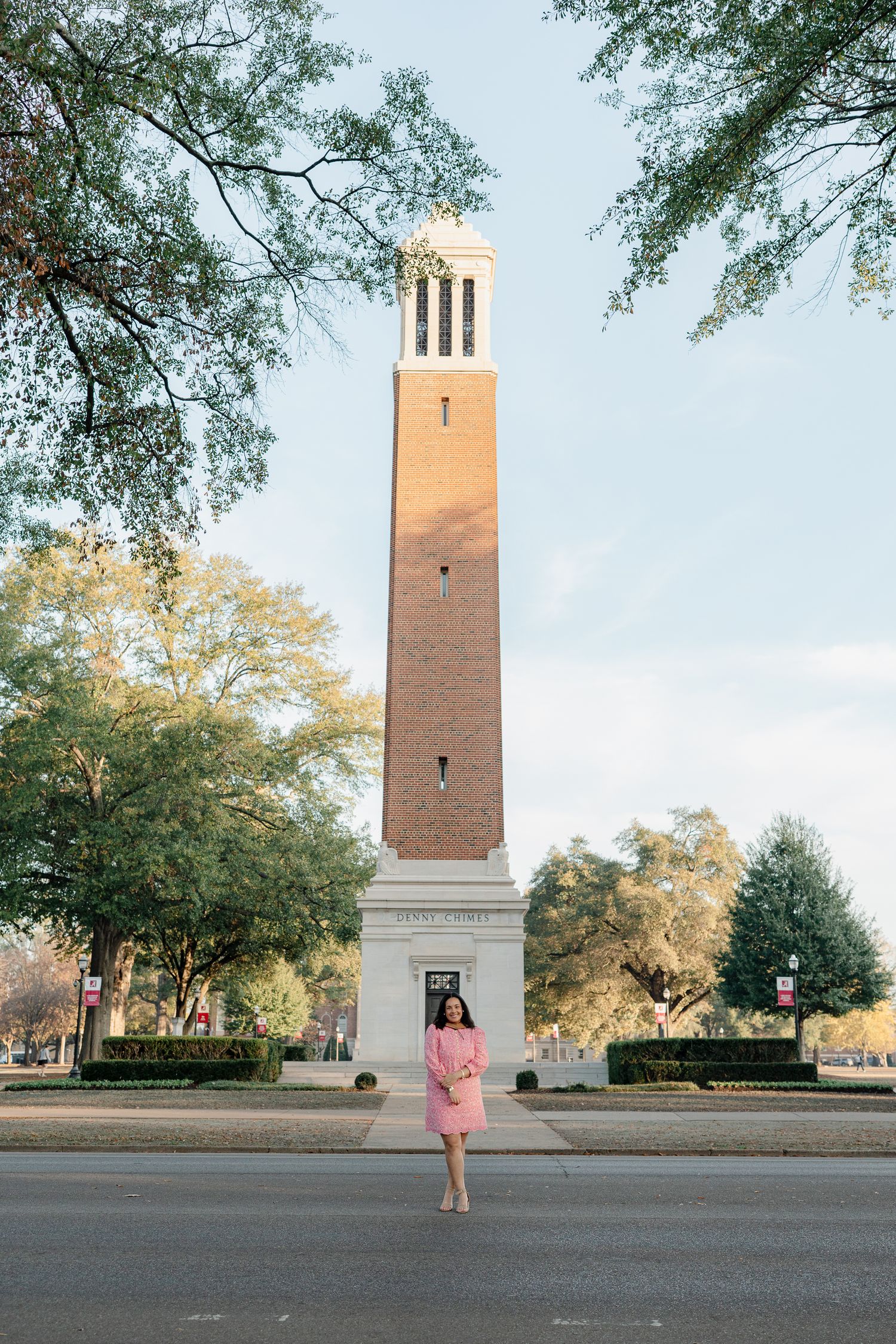 A graduate poses in front of Denny Chimes tower on a university campus.