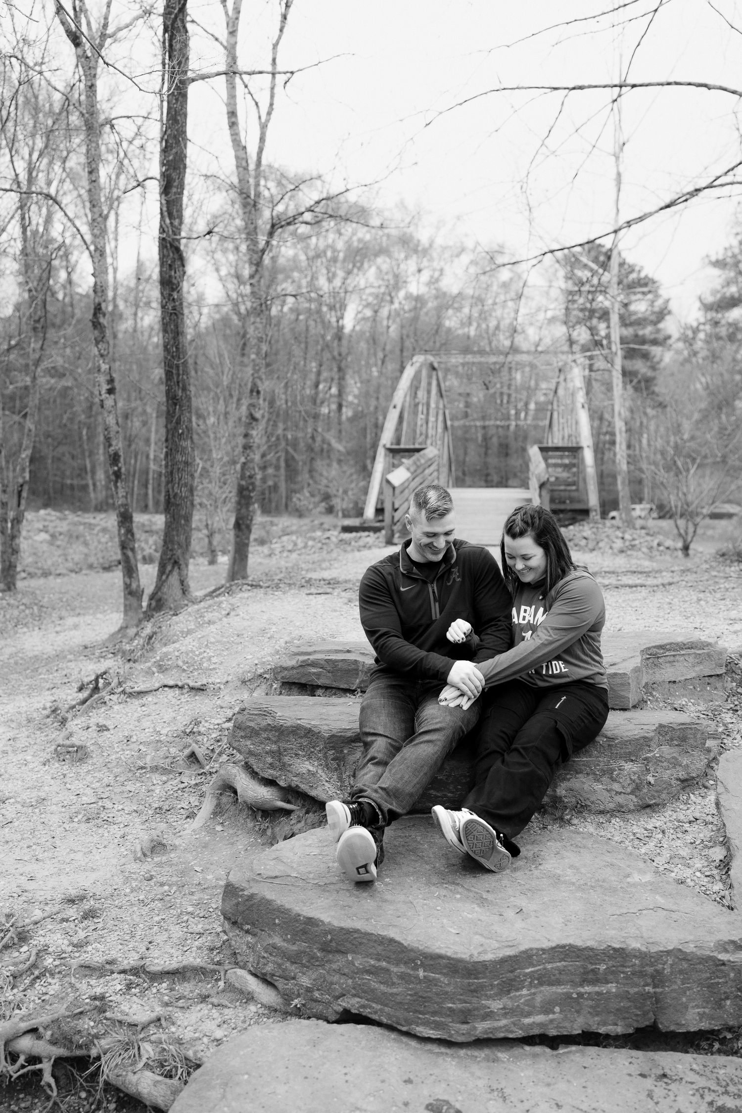 A couple relaxes on a large boulder in a winter forest landscape.