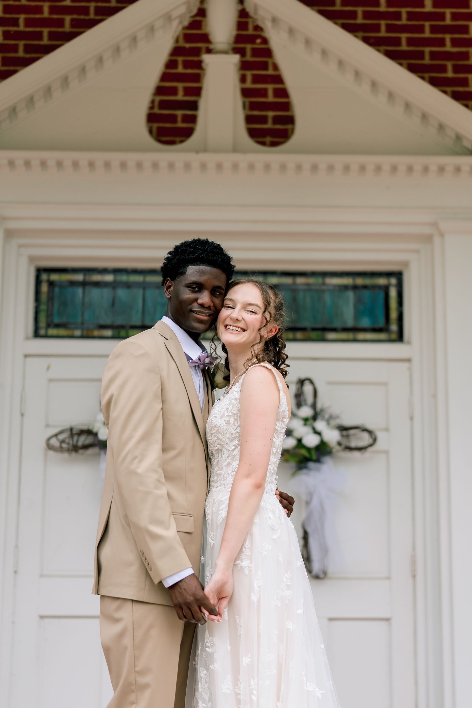 Interracial wedding couple holding hands and embracing in front of a white church door.